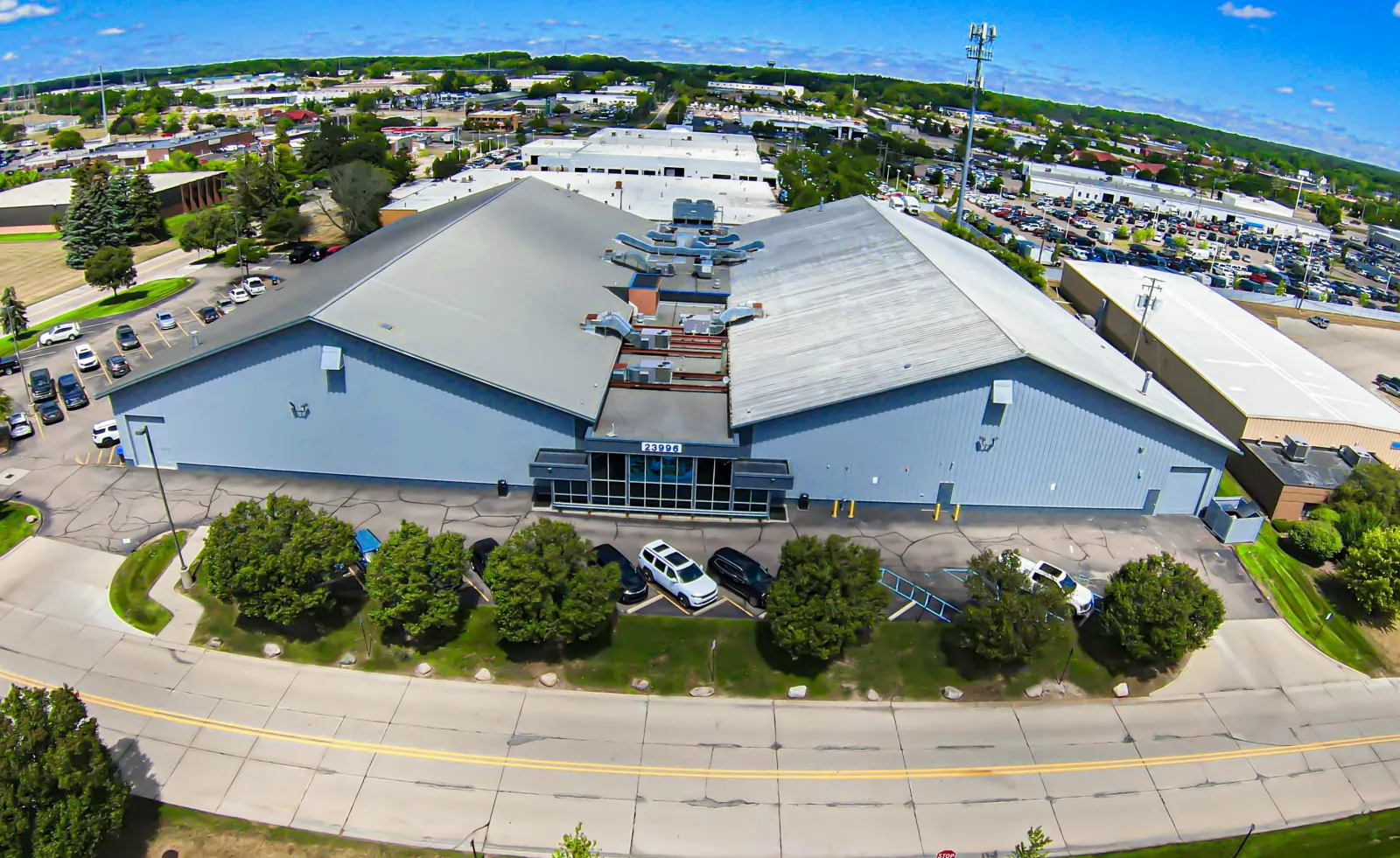 Aerial view of the arena's twin gabled blue-grey halls from Freeway Park Drive, with the glass entrance marked 23996 between them and the parking lot around it. — Suburban Ice Farmington Hills