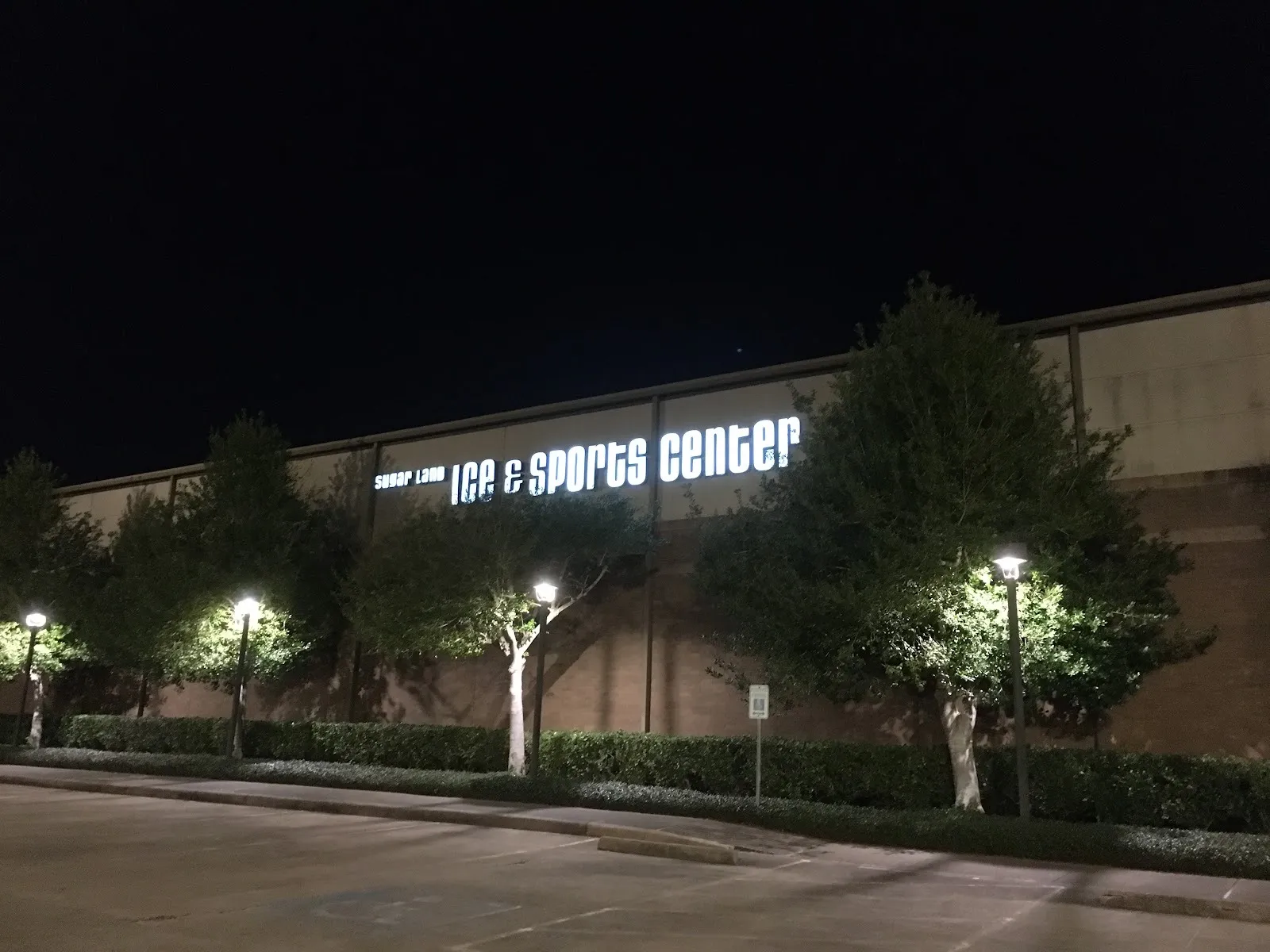 The Sugar Land Ice & Sports Center at night, its name lit along the long brick wall above a row of trees and lamps — Sugar Land Ice and Sports Center