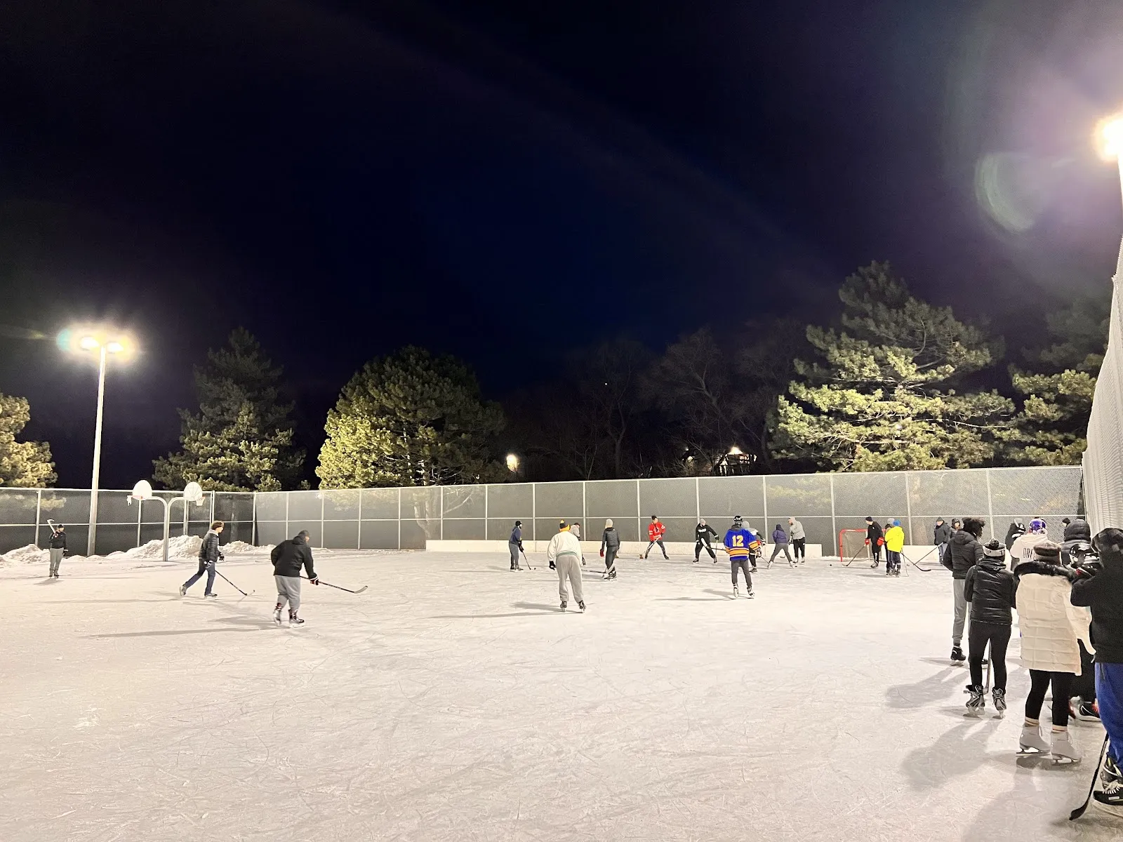 The Summerlea Park rink at night under floodlights with skaters across the ice and trees behind — Summerlea Park Outdoor Ice Rink