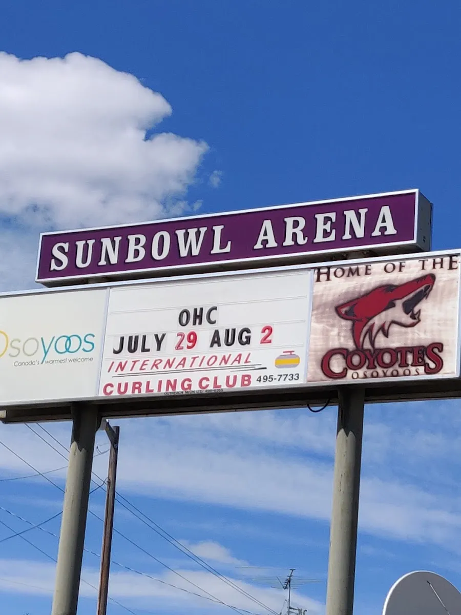 El cartel de carretera del Sunbowl Arena con letras moradas y un panel de mensajes que anuncia el International Curling Club y los Osoyoos Coyotes, bajo un cielo azul brillante. — Sun Bowl Arena