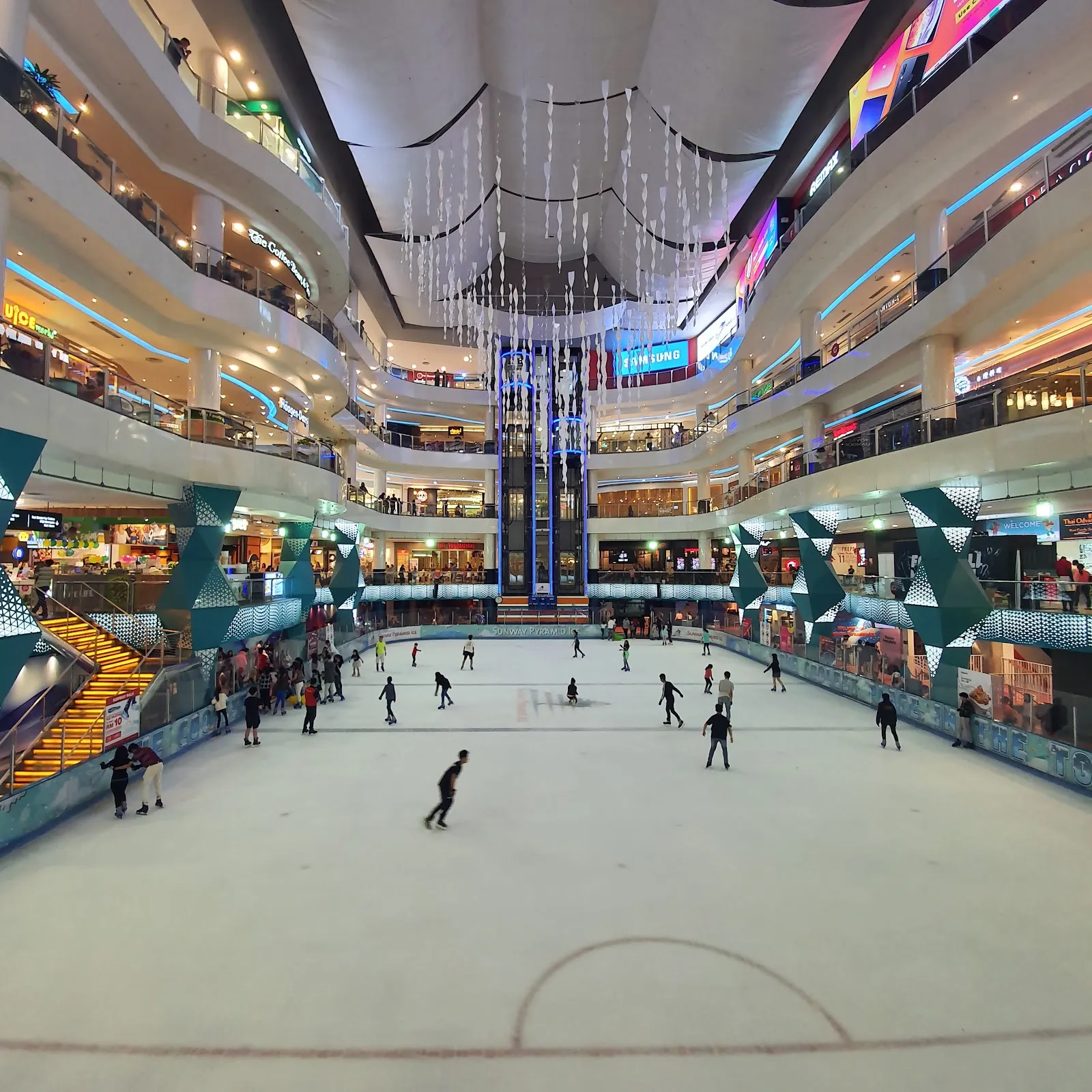 The sheet seen from the upper floors of Sunway Pyramid, with the lit galleries rising around it and skaters spread across the ice. — Sunway Pyramid Ice