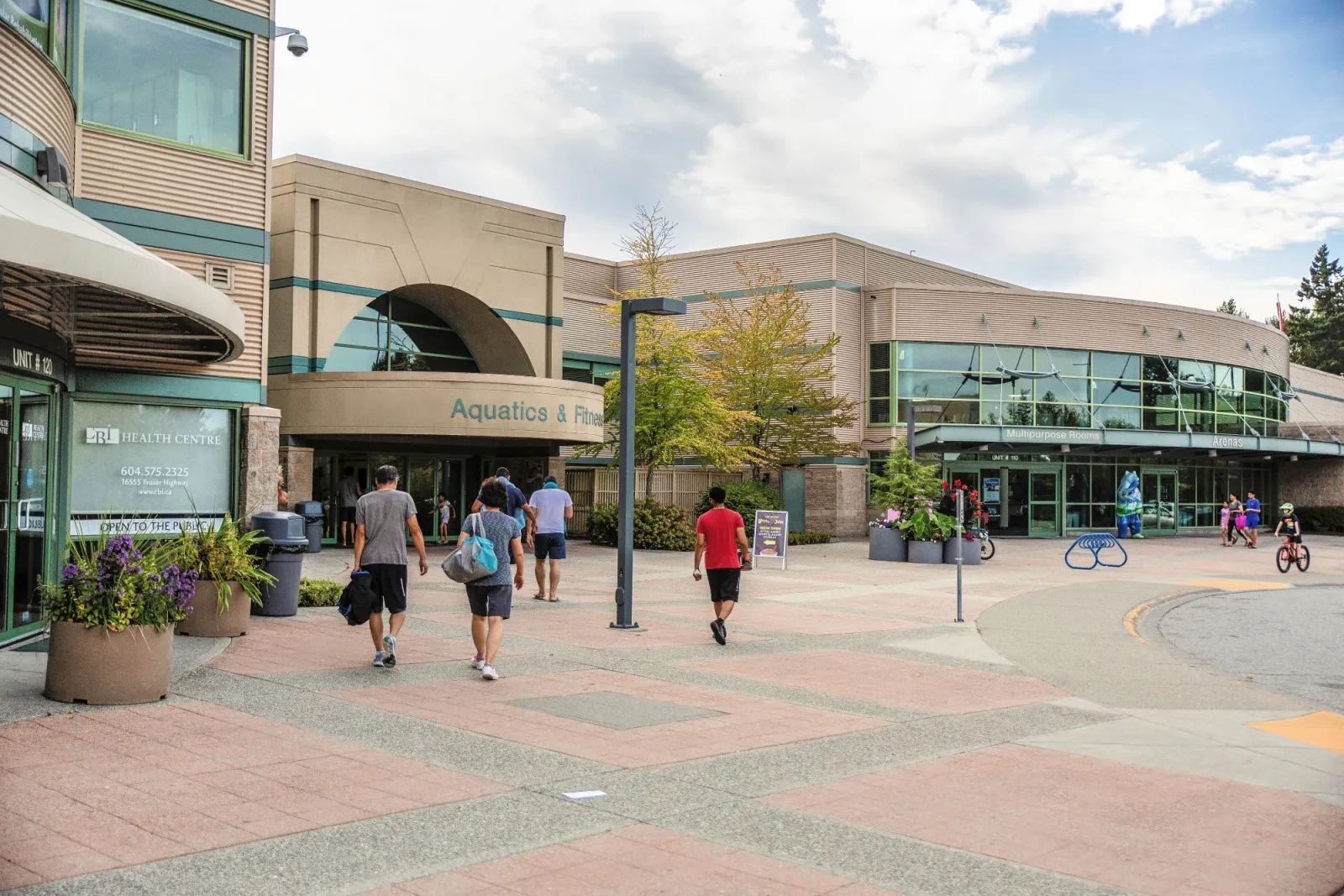 Exterior plaza of Surrey Sport & Leisure Complex, with the Arenas entrance and Multipurpose Rooms doors visible on the right and the Aquatics & Fitness entrance at center. — Surrey Sport & Leisure Complex Arena