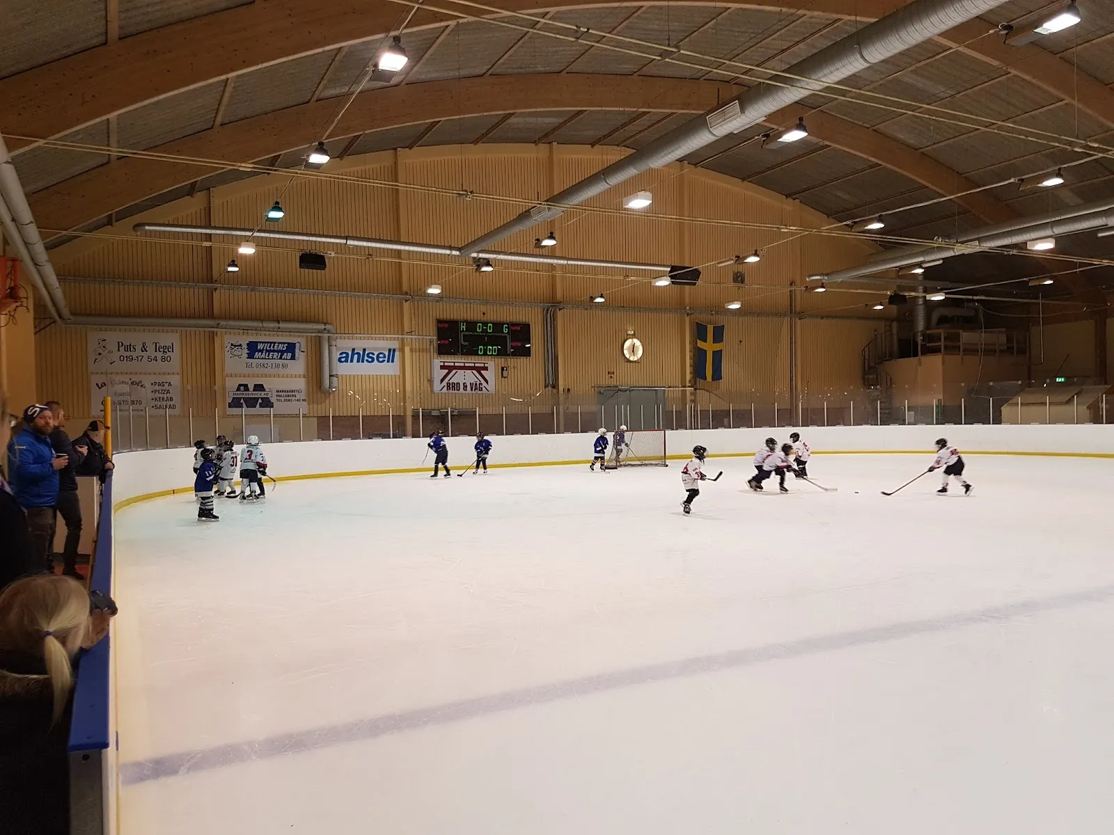 En hockeymatch på isen i Sydnärkehallen i Hallsberg, sedd från läktaren under trätaket och strålkastarna. – Sydnärkehallens ishall