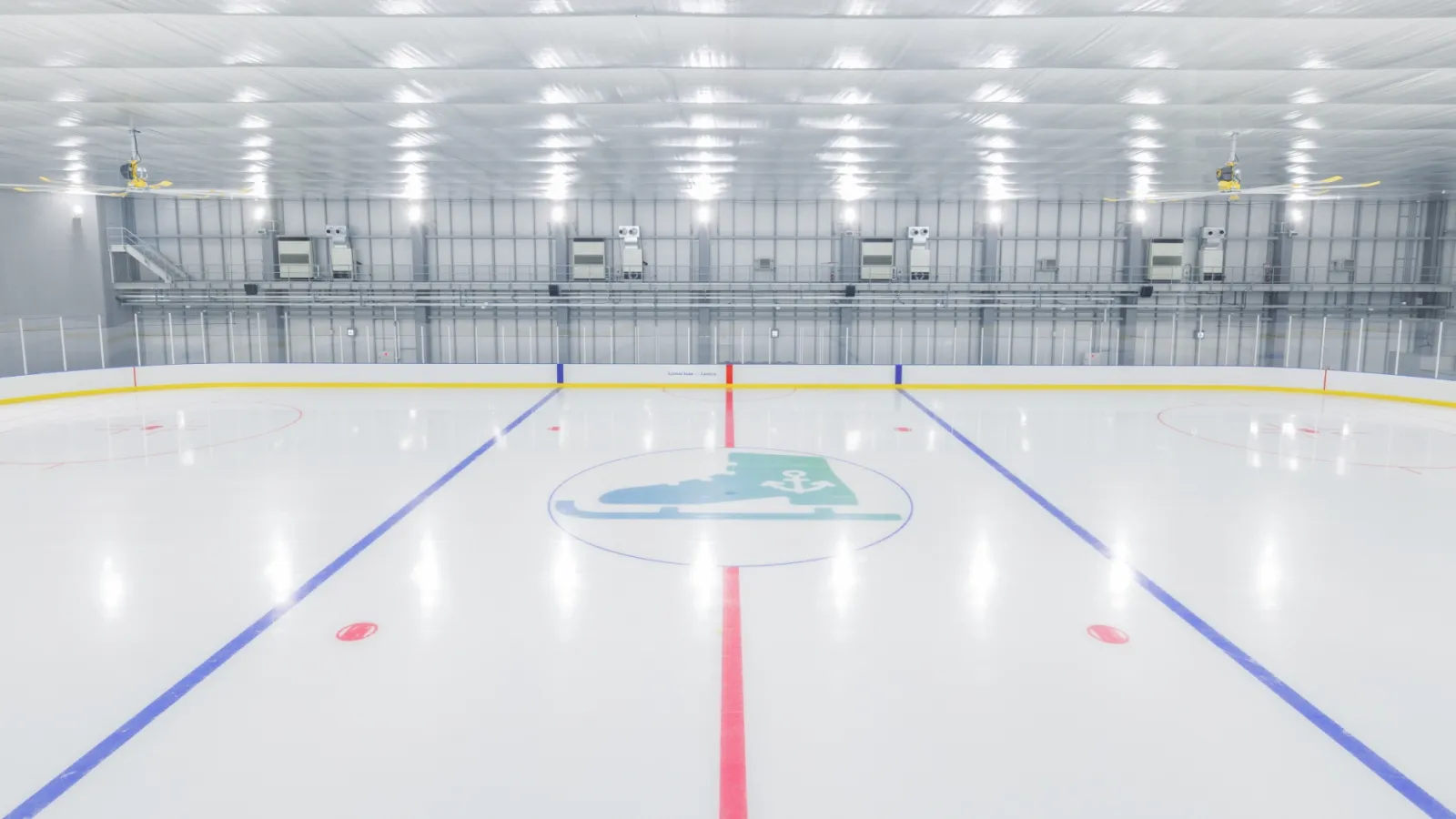 The empty ice sheet of Sysmex Kobe Ice Campus with its blue lines, centre-ice emblem and the white hall with ceiling lights. — Sysmex Kobe Ice Campus