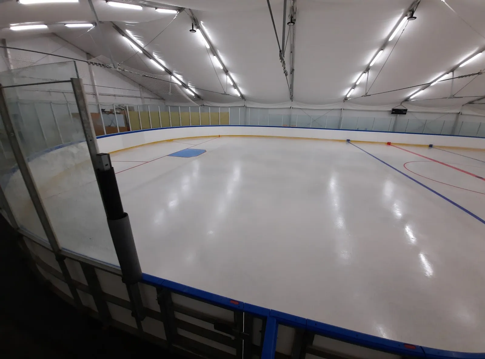 The wide indoor ice at Szarvas under bright ceiling lights, with the boards and a rink-side wall along one side. – Szarvasi Jégpálya