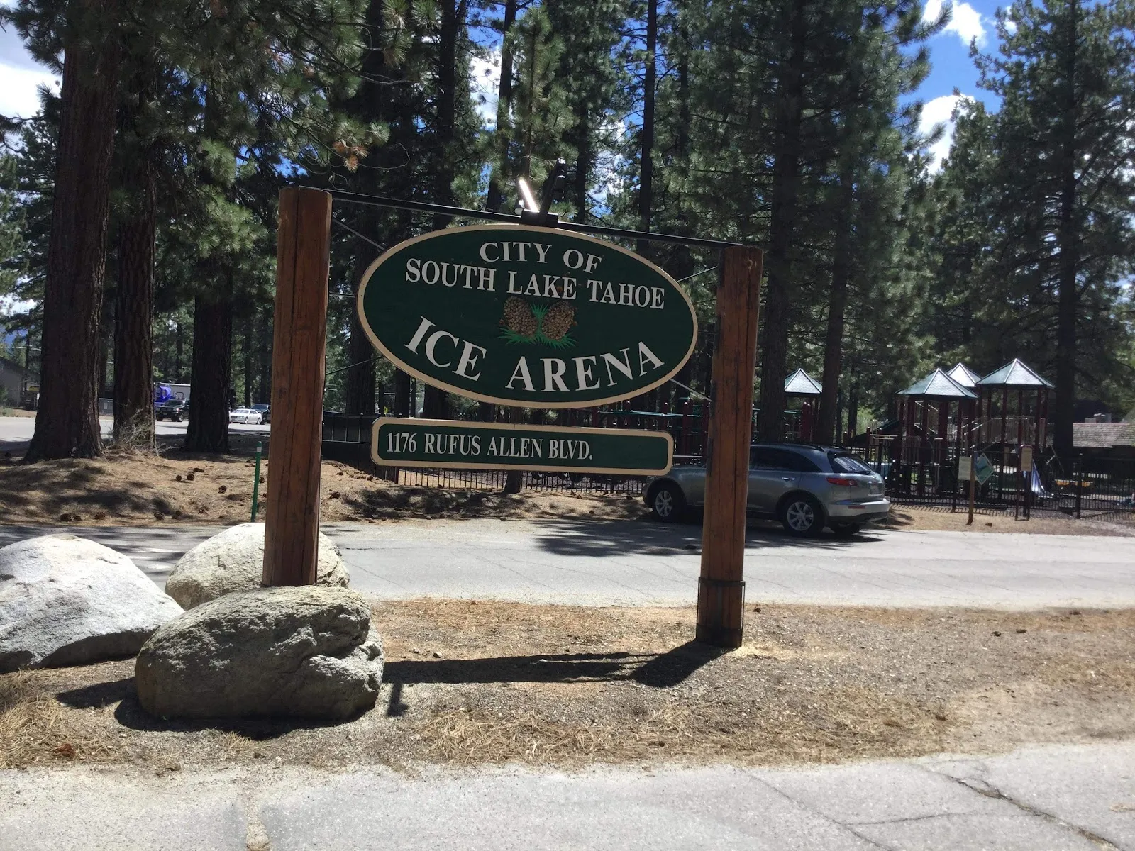 The wooden City of South Lake Tahoe Ice Arena sign on Rufus Allen Boulevard, framed by boulders and tall pines — Tahoe Ice Arena