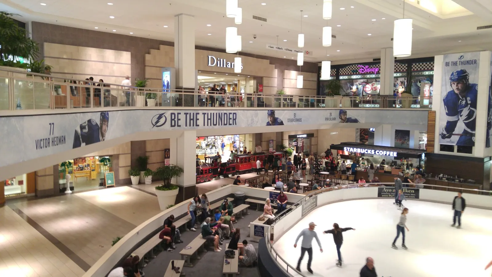 La pista del centro comercial vista desde el nivel superior, con patinadores en el hielo, una manta de los Lightning de "Be the Thunder" y locales comerciales alrededor del atrio. — Tampa Bay Skating Academy (Countryside Mall)