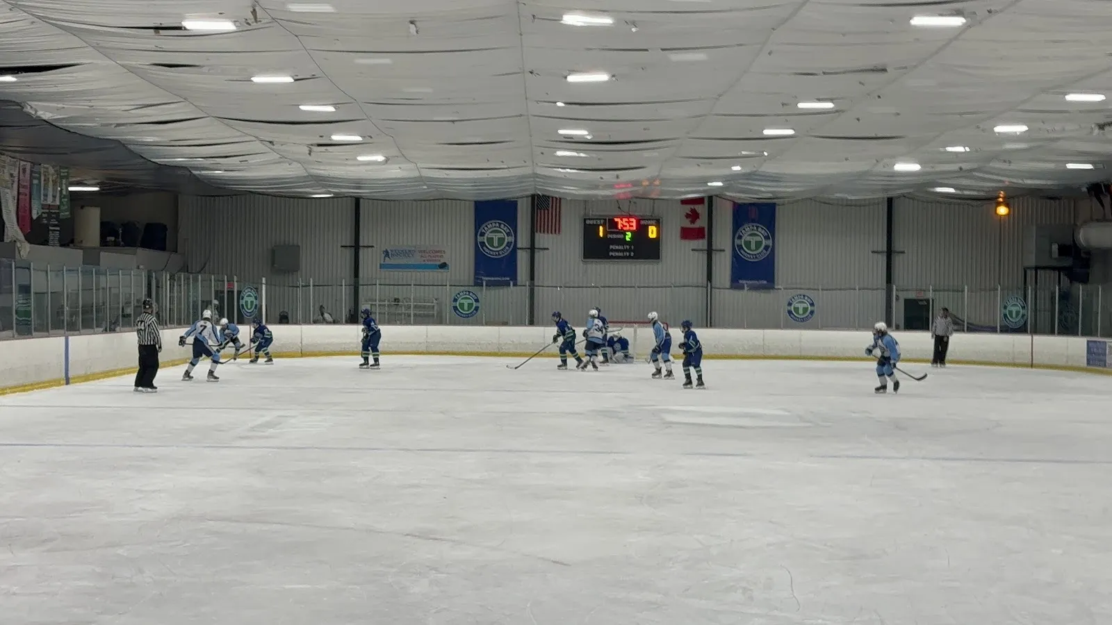 Una vista amplia a través de la pista, con patinadores repartidos a lo largo de las vallas del fondo bajo un techo plano y banderines colgados en la pared del extremo. — Tampa Bay Skating Academy (Oldsmar)