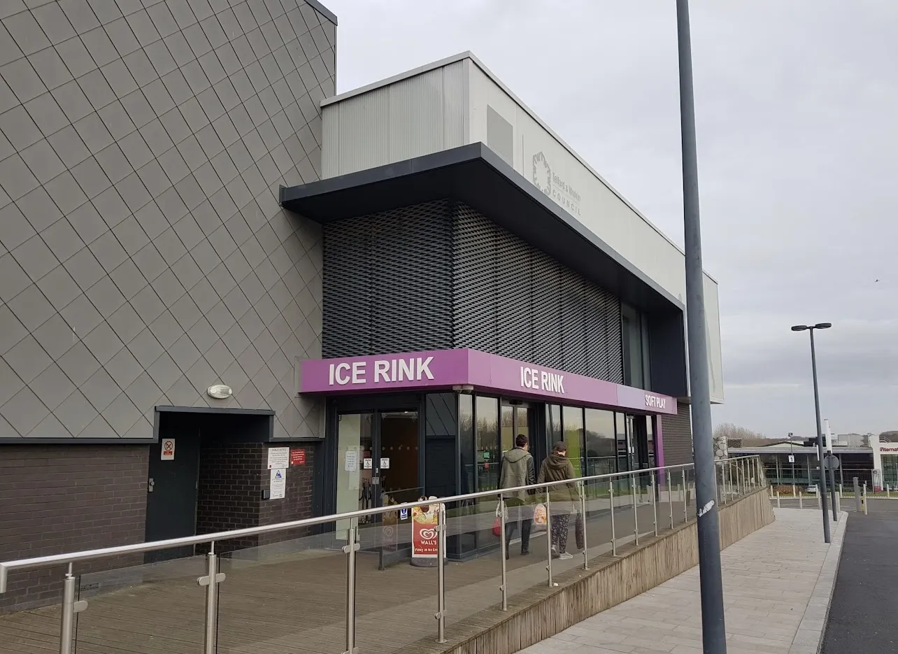 The grey cladded corner of the building with the pink-fronted 'ICE RINK' entrance canopy and glazed doors at pavement level. — Telford Ice Rink