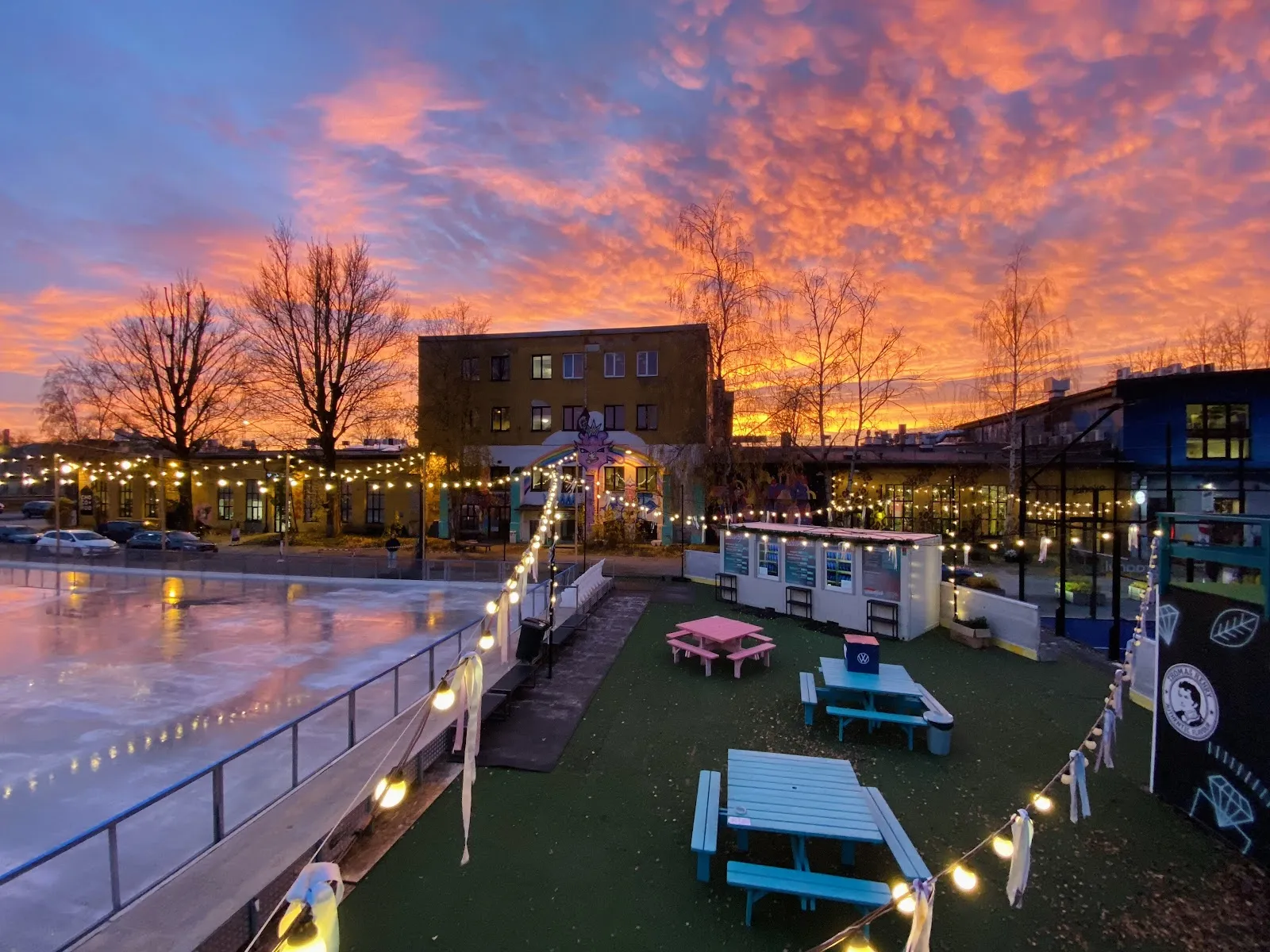 The Telliskivi ice rink edge, picnic tables and the creative-quarter buildings at dusk — Telliskivi uisuväljak