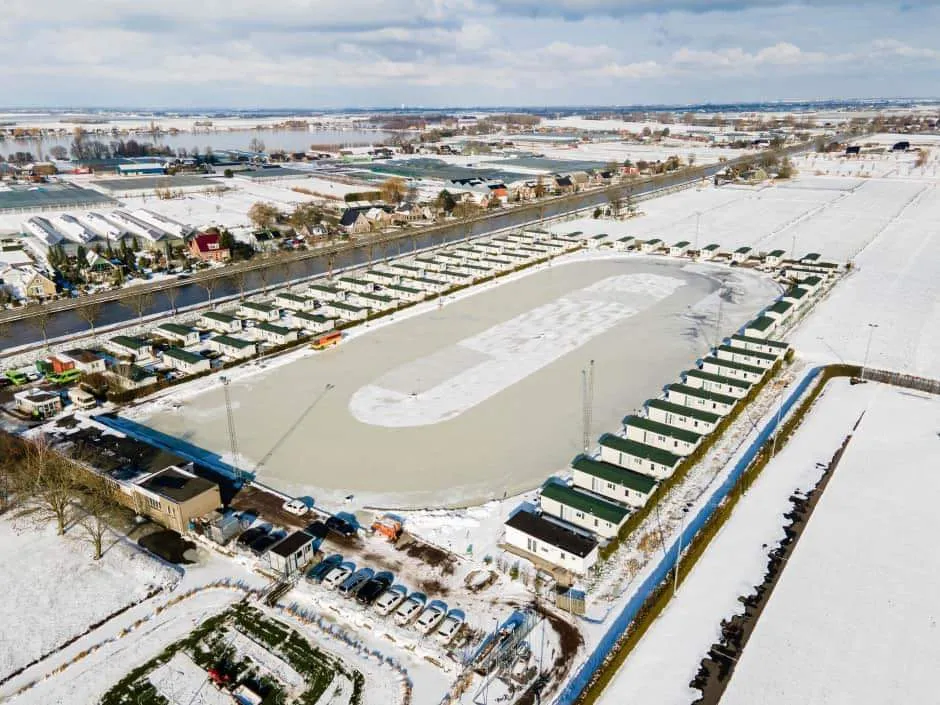Aerial view of the Ter Aarse IJsclub natural-ice track under snow, with the clubhouse area and parking along its edge. — Landijsbaan Ter Aar (Ter Aarse IJsclub)