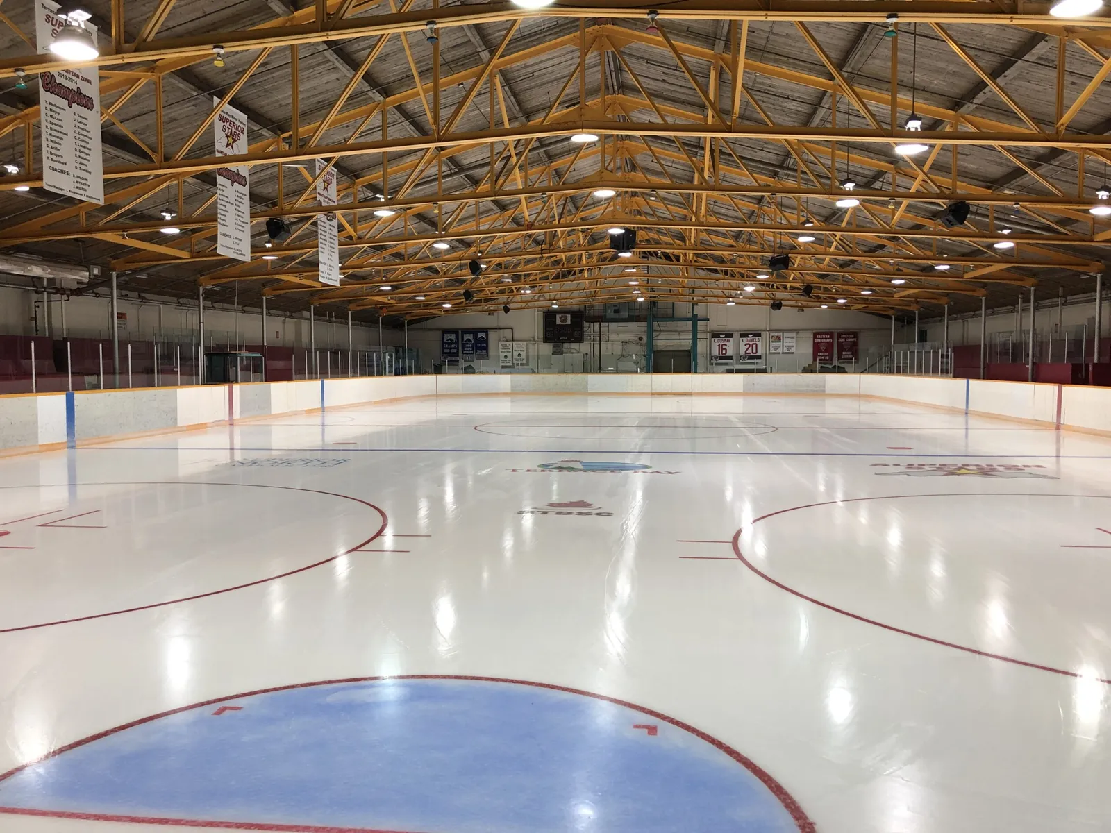 The ice surface of the Terrace Bay Memorial Arena with its red and blue lines, seen from the end of the rink under the wooden roof. — Terrace Bay Memorial Arena