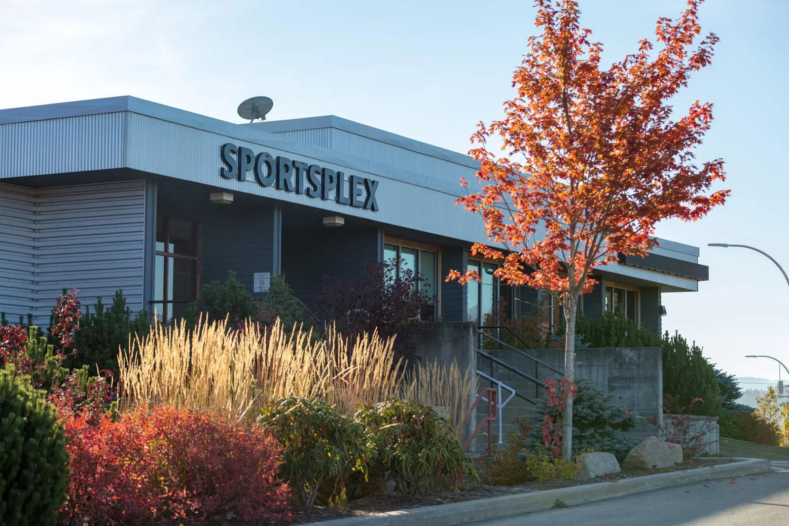 The Terrace Sportsplex entrance, its name across the grey facade, behind autumn shrubs and a red-leaved tree. — Terrace Sportsplex