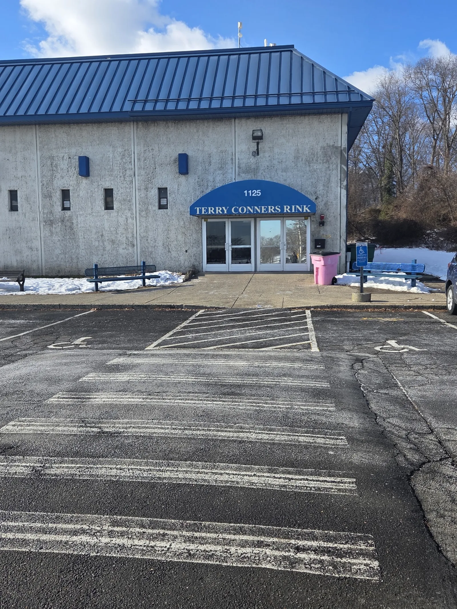 The concrete building with a blue metal roof and a blue awning over the entrance reading 1125 Terry Conners Rink, on a sunny winter day. — Terry Conners Rink