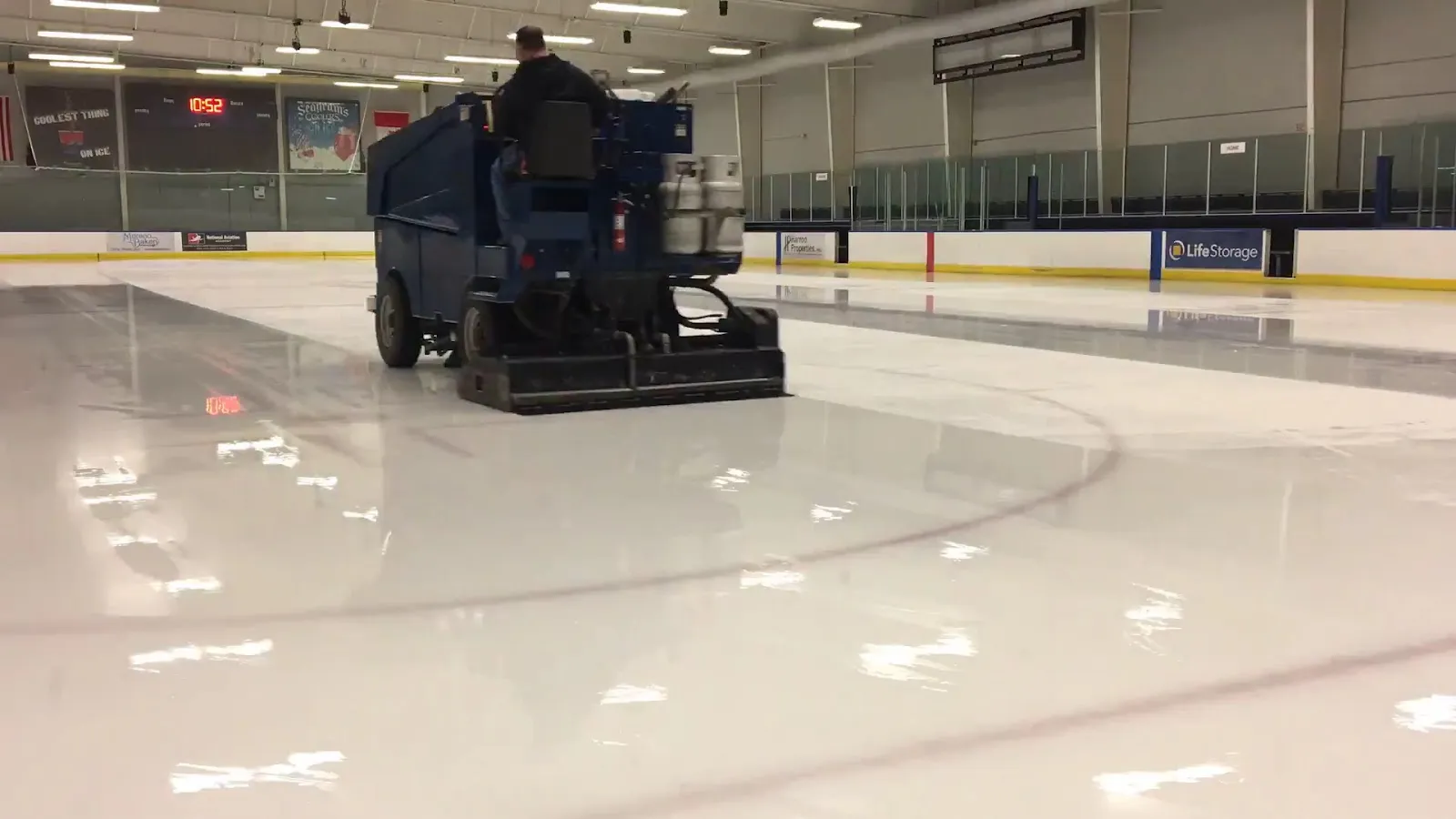 Fresh ice at TGH Ice Plex with the resurfacer on the sheet and the glass and sponsor boards behind — TGH Ice Plex