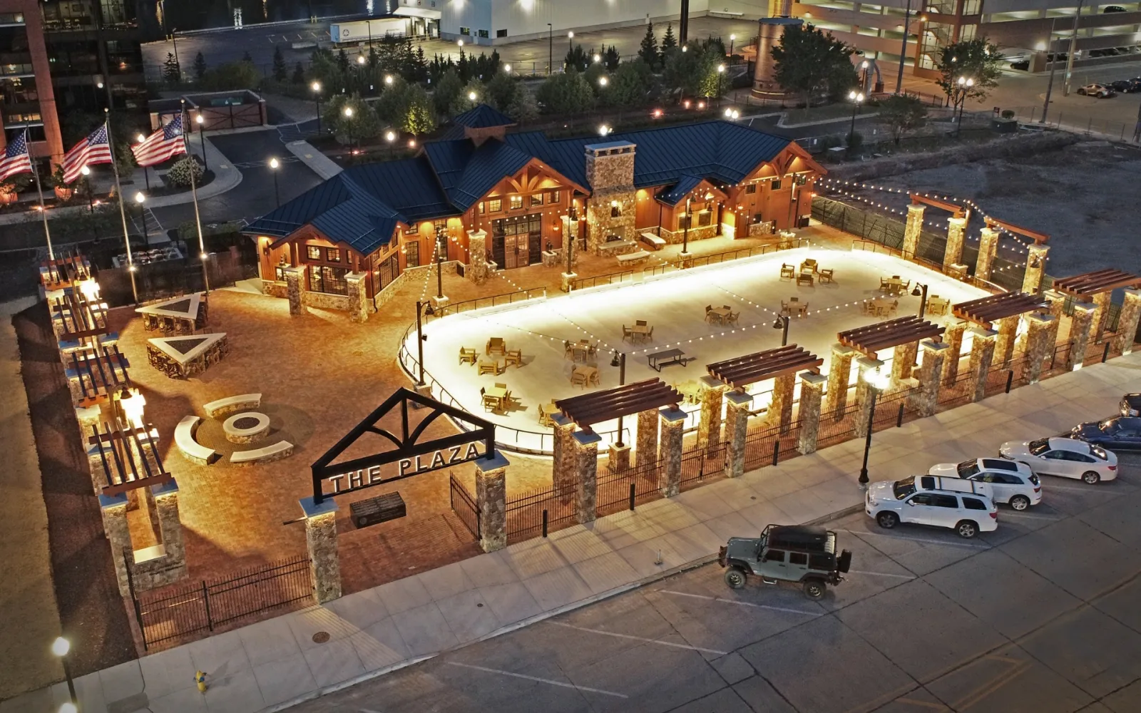 The Plaza at Gateway Park from above at night, with the timber-and-stone skate house, the entrance gate and the rink area lit in front of the building. — The Plaza at Gateway Park
