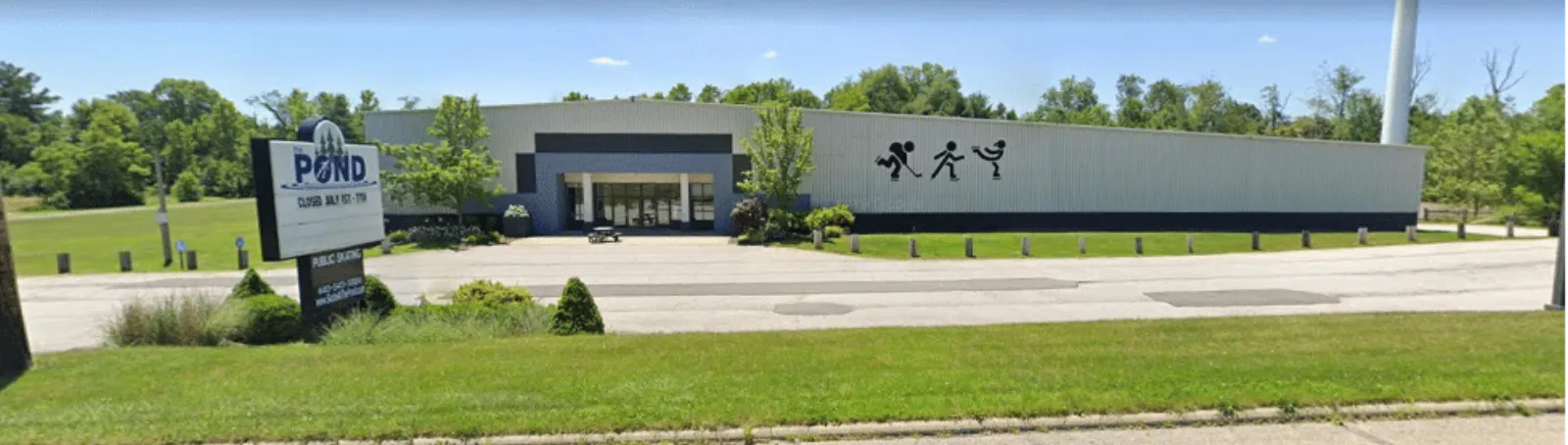 Wide daytime view of the low metal-panel building from the parking lot, with a freestanding "POND" sign out front and skating/running figure icons painted on the fascia above the entrance. — The Pond Ice Rink & Sports Complex