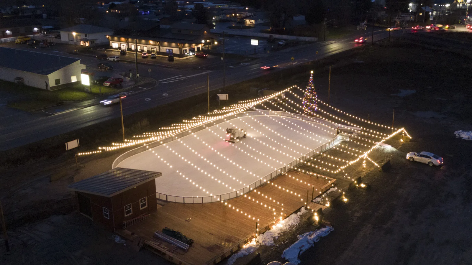 The Pond in Ponderay lit up after dark, seen from above beside the highway — The Pond Ice Rink