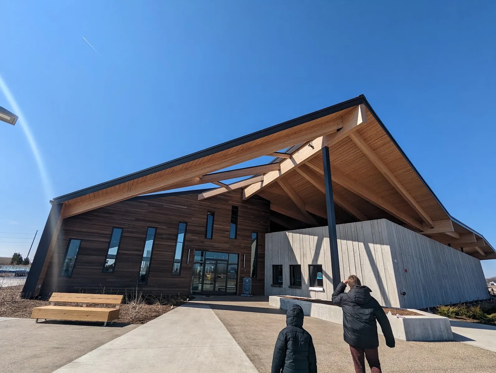 El Market Hall, el edificio con techo de madera junto a The Ribbon donde se registran los patinadores, visto desde su andador frontal bajo un cielo despejado. — The Ribbon at Glass City Metropark