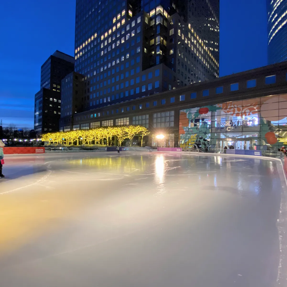 The rink at dusk in front of the Brookfield Place buildings, with the empty ice in the foreground — The Rink at Brookfield Place