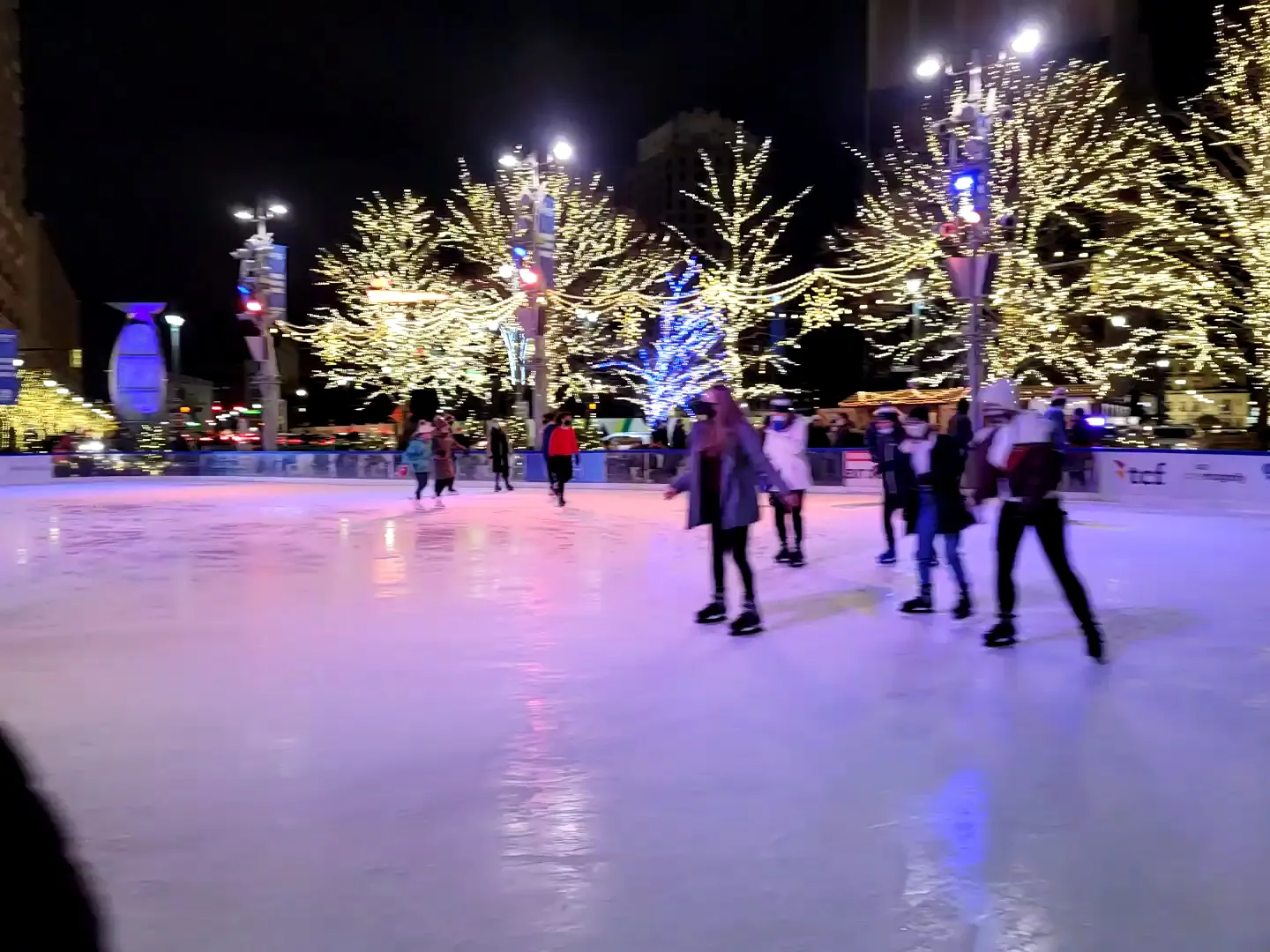 Evening skaters on the lit Rink at Campus Martius Park among the downtown towers — The Rink at Campus Martius Park