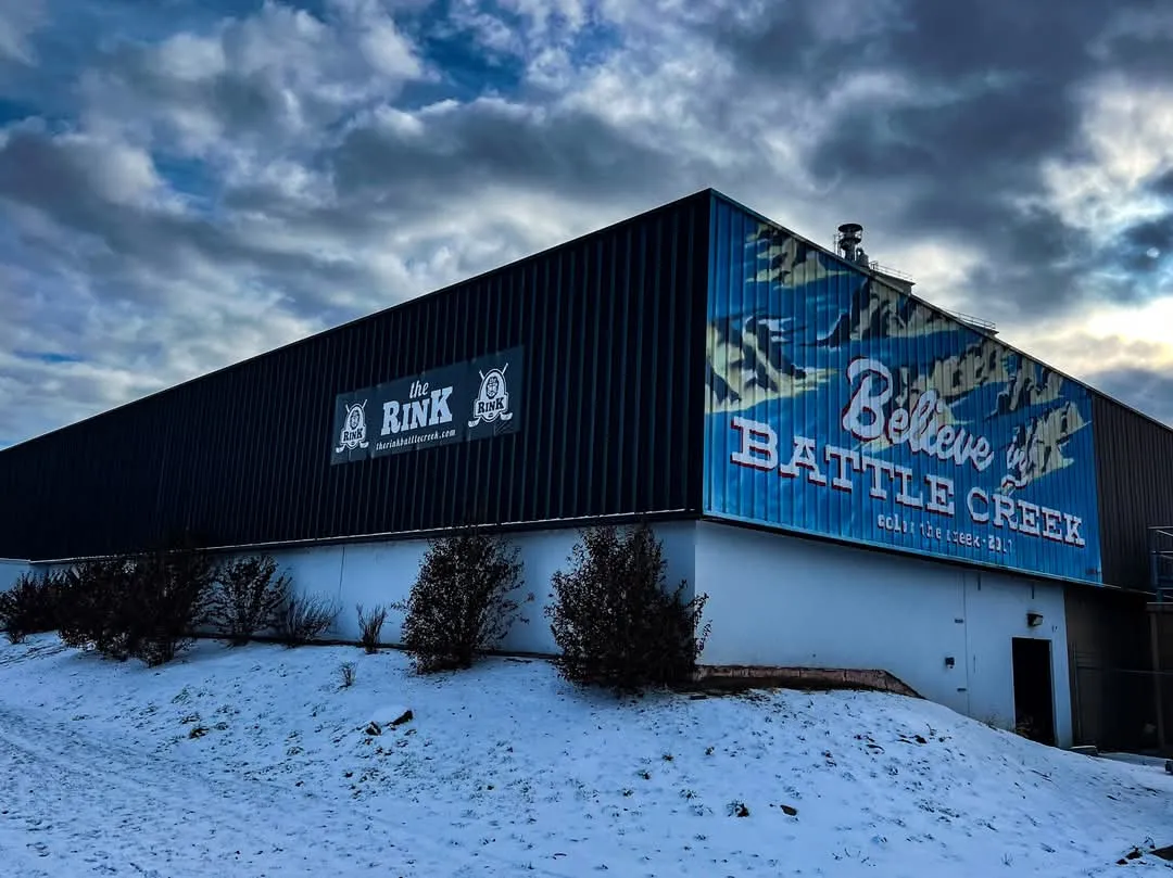 The arena's dark steel building under a winter sky, with The Rink sign and a mural reading "Believe Battle Creek" along the wall. — The Rink Battle Creek