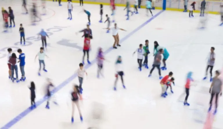 Skaters across the main sheet during a public skate at The Rink on the Beach, with the blue line and boards behind them. — The Rink on the Beach