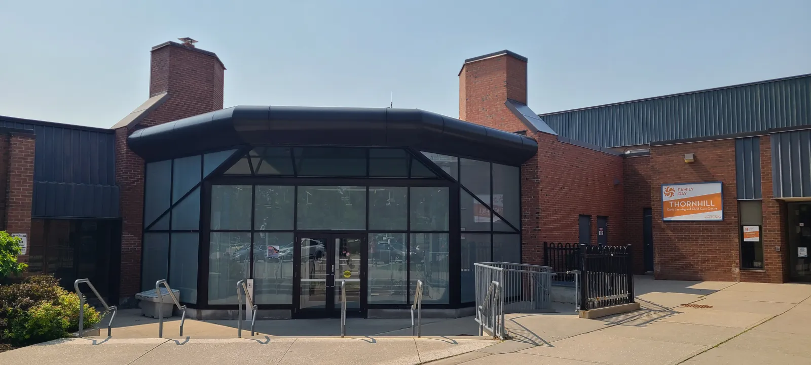Front entrance of Thornhill Community Centre, a brick building with a glass-and-black-metal canopied entryway and twin brick chimneys, with a "Thornhill Early Learning and Child Care Centre" sign to the right of the doors. — Thornhill Community Centre