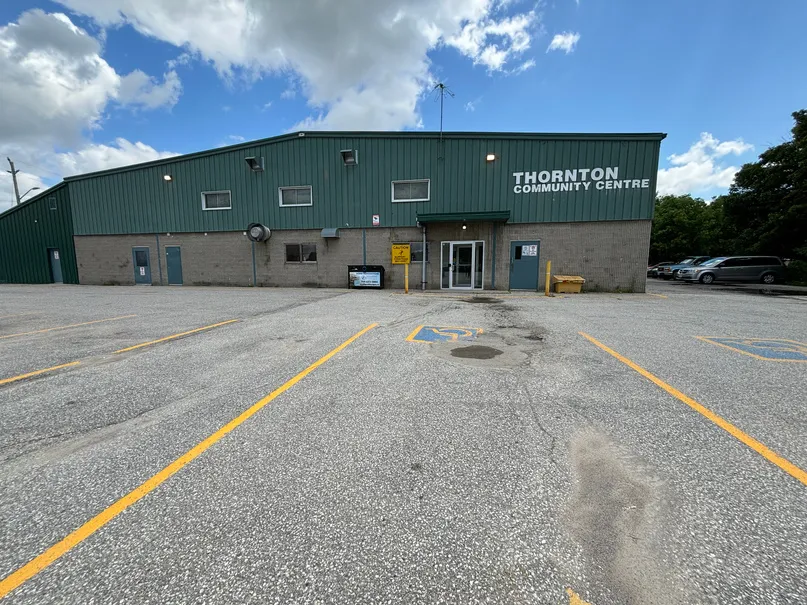 El frente del Thornton Community Centre: un edificio de metal revestido en verde con base de bloques, el nombre en el muro sobre la entrada y un estacionamiento pavimentado al frente. — Thornton Community Centre (Essa)