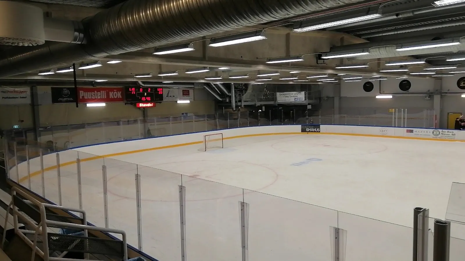 Wide view over the ice sheet and boards of the hall at Åva in Täby (Skanskahallen), with the scoreboard at the far end – Tibble ishall