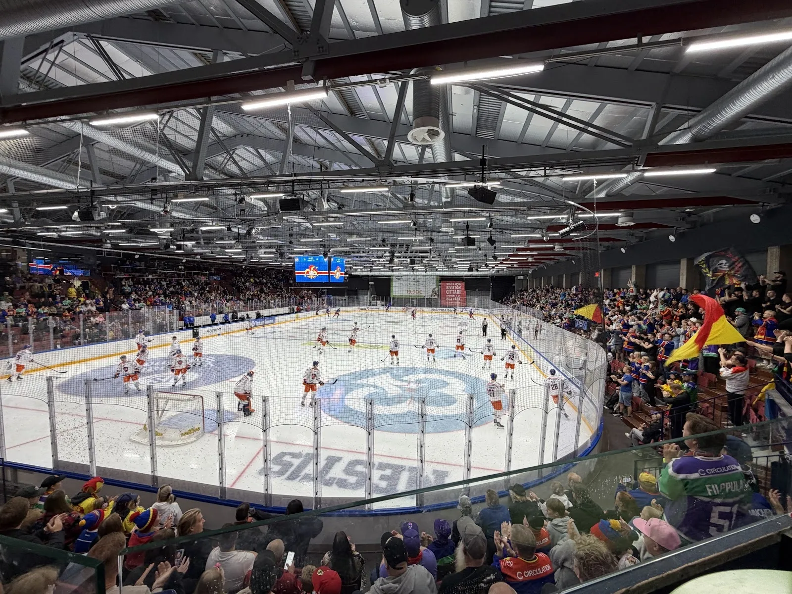 Ottelu Tikkurila Areenalla katsomosta kuvattuna: katsojien ympäröimä jääkenttä ja kattovalot yläpuolella. – Tikkurila Areena