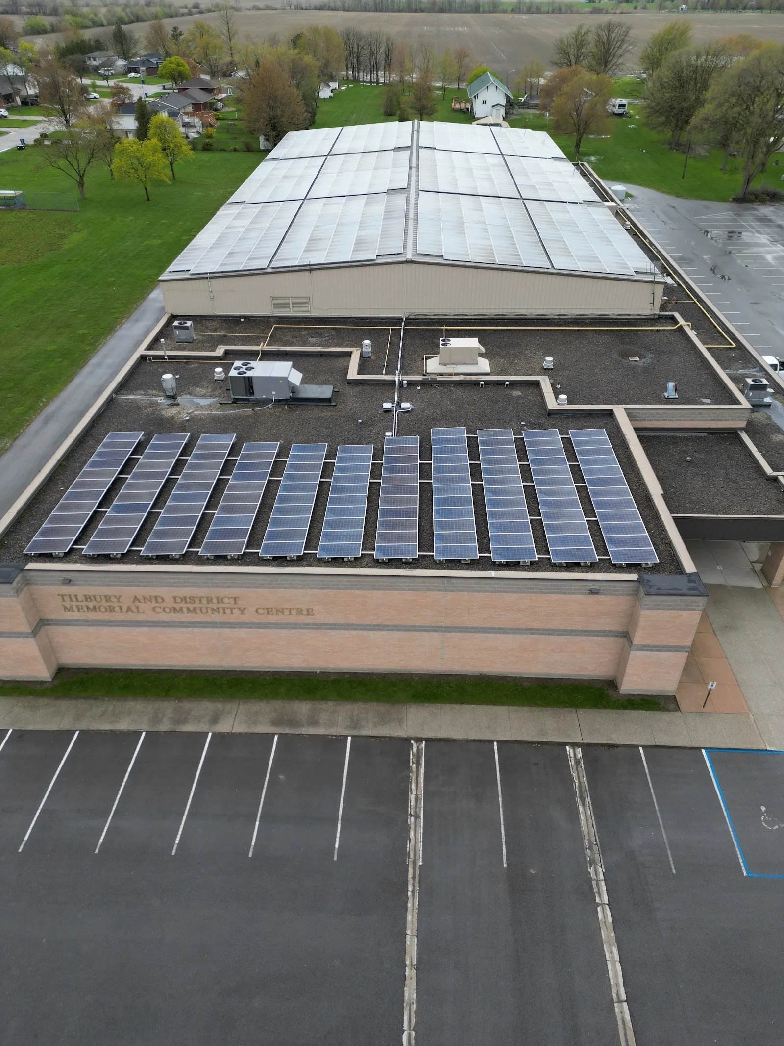 An aerial view of the Tilbury Arena's long flat roof with solar panels and a car park along one side. — Tilbury Arena
