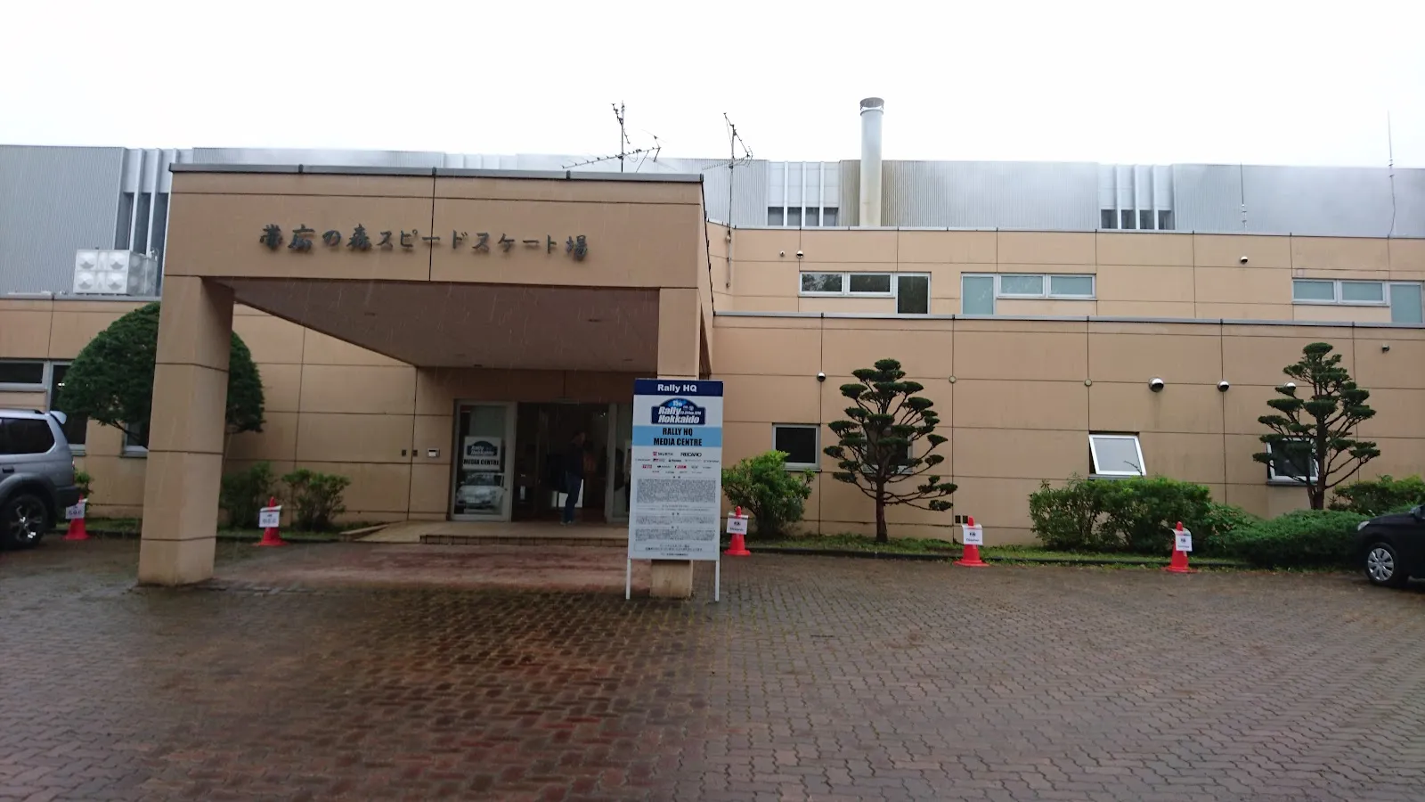 十勝オーバルのレンガ舗装の前庭と庇のある入口。壁の看板には建物の旧称「帯広の森スピードスケート場」が見えます。 — Tokachi Oval
