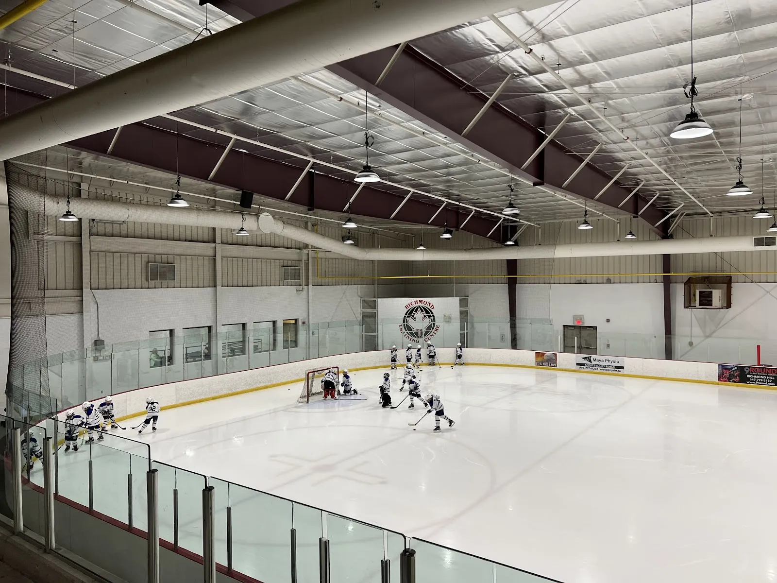 One of the two rinks from the upper corner: a hockey group at the far net and the boards running the length of the pad. — Tom Graham Arena Complex (Richmond Hill)