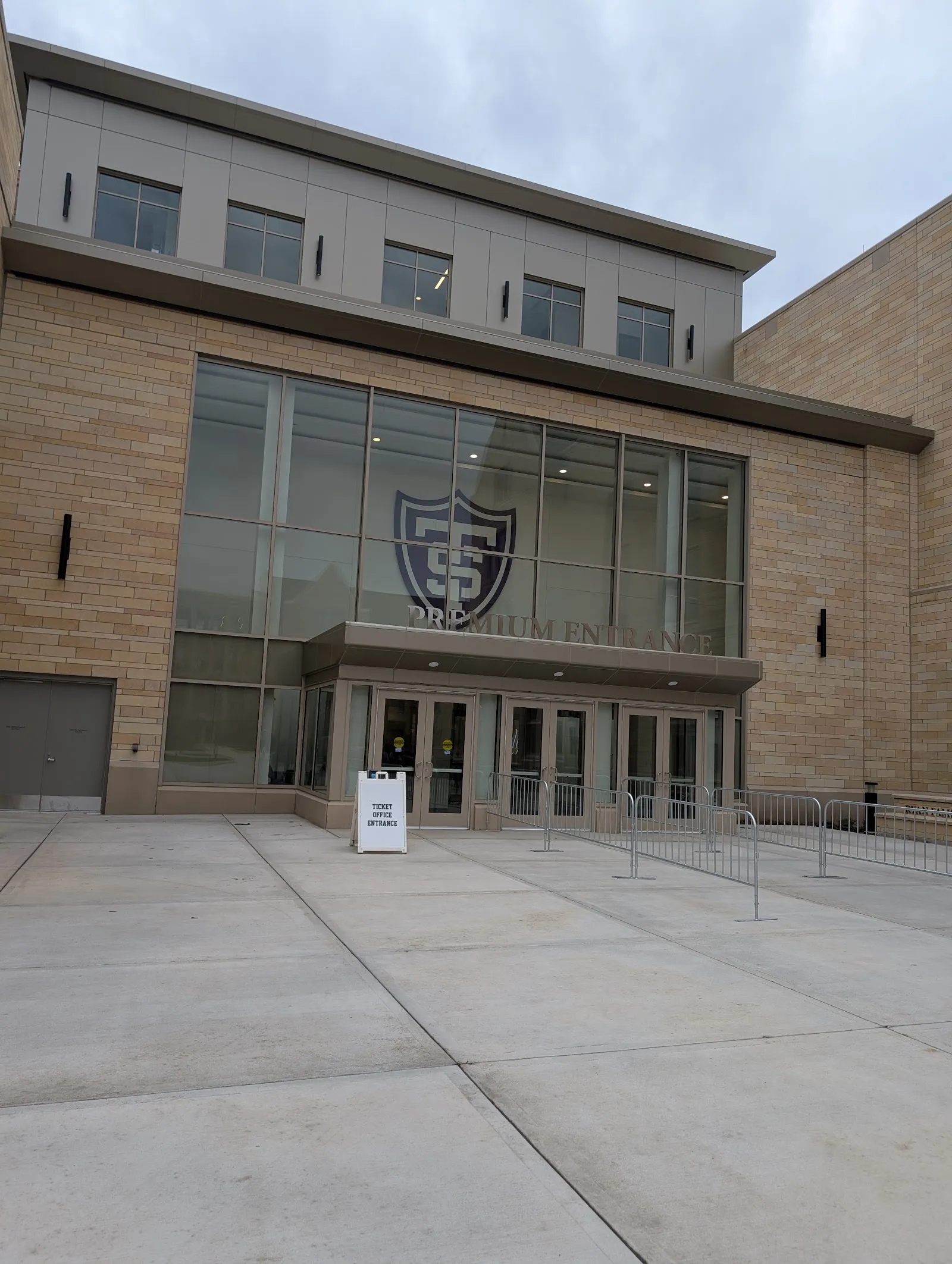 The stone and glass entrance of Lee and Penny Anderson Arena at the University of St. Thomas, with the St. Thomas shield over the doors and the concrete plaza in front — Tommie Iceplex at Lee & Penny Anderson Arena