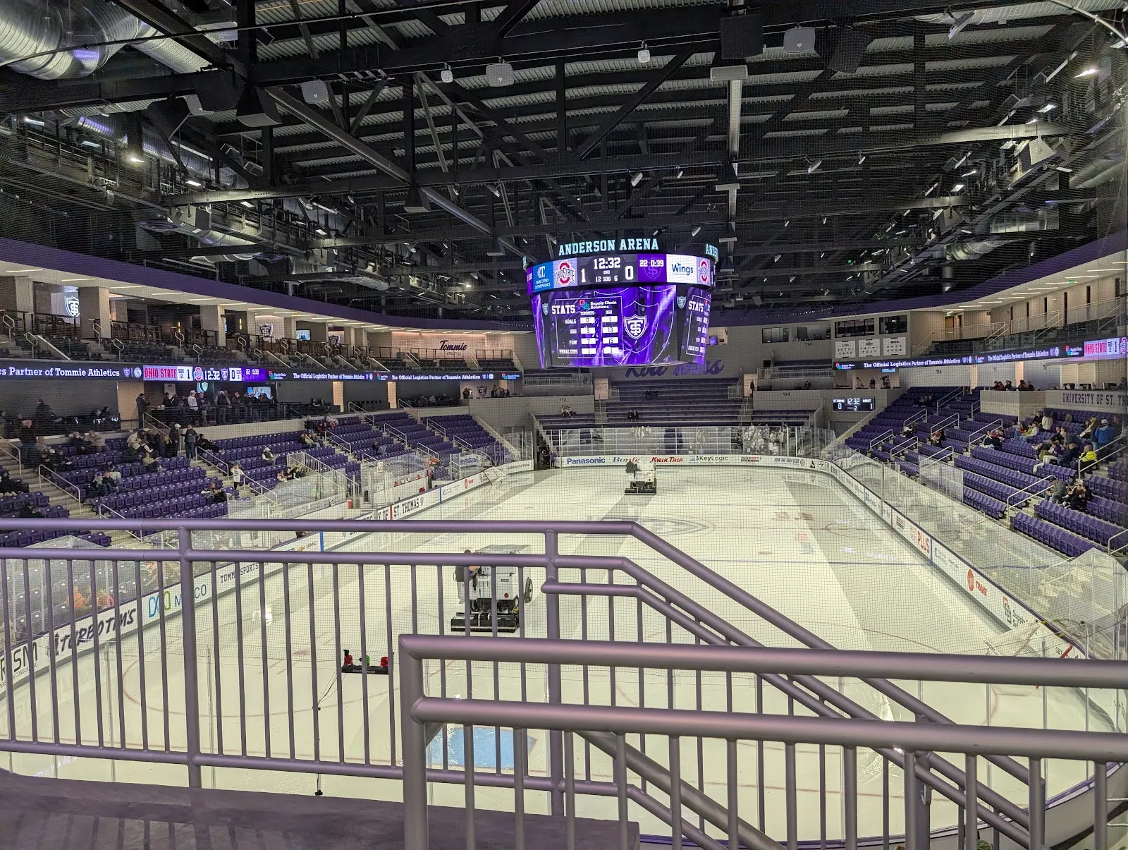 The ice in Lee and Penny Anderson Arena seen from the upper concourse, with the purple seating bowl, the centre-hung scoreboard and the resurfacer on the sheet — Tommie Iceplex at Lee & Penny Anderson Arena