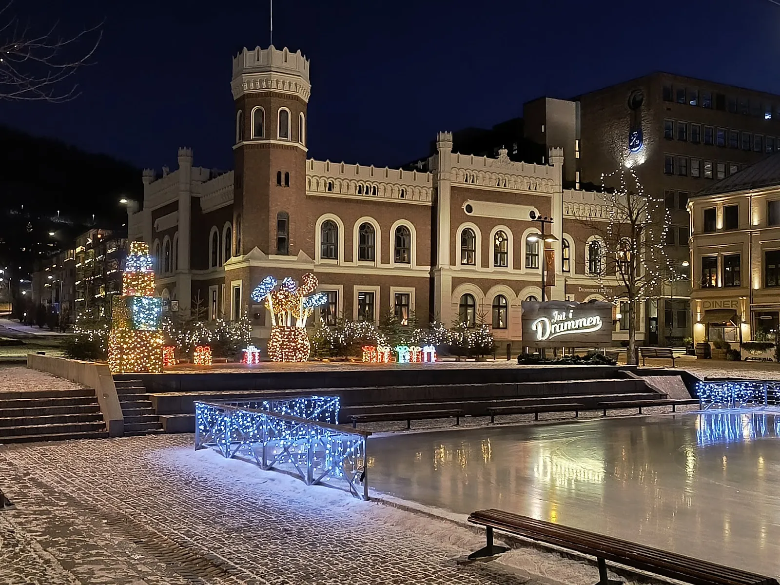 Torgisen på Bragernes torg om natten, med den opplyste isen ved siden av Drammens gamle rådhus og julelysene. — Torgisen
