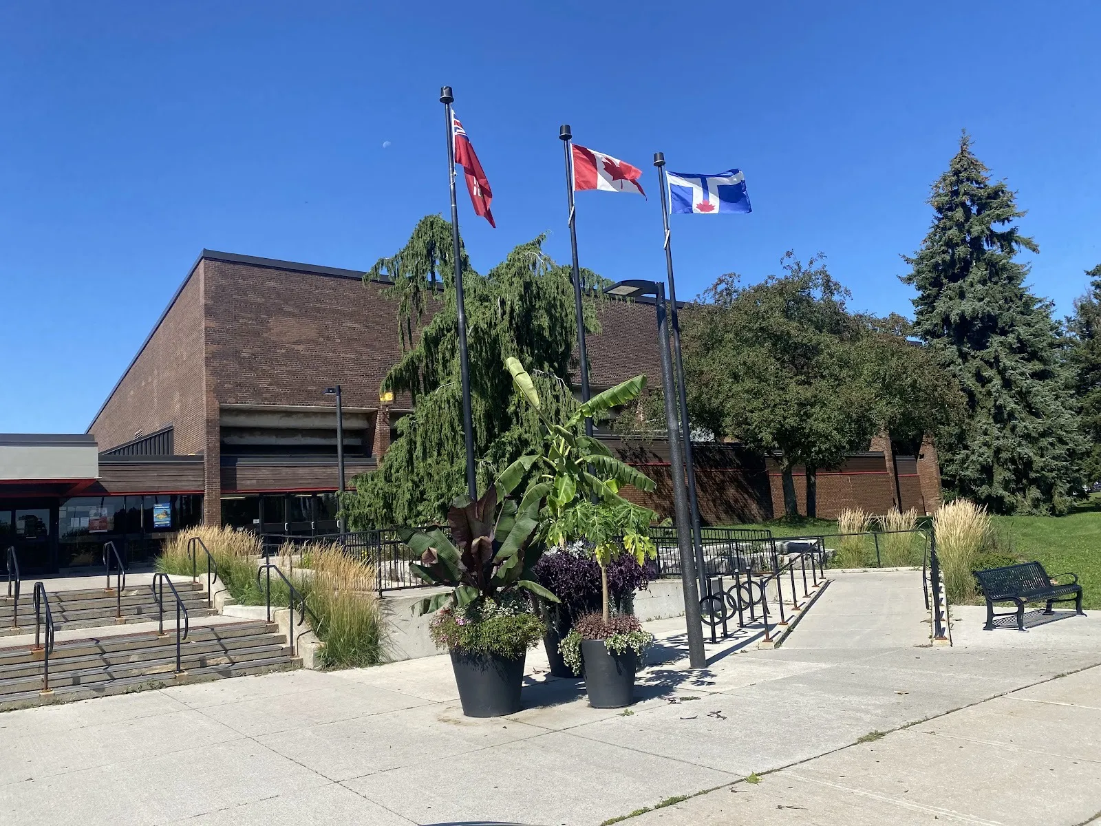 El Scarborough Centennial Recreation Centre, de ladrillo, en Ellesmere Road, con banderas y jardineras junto a los escalones de la entrada en un día soleado — Centennial Recreation Centre - Scarborough