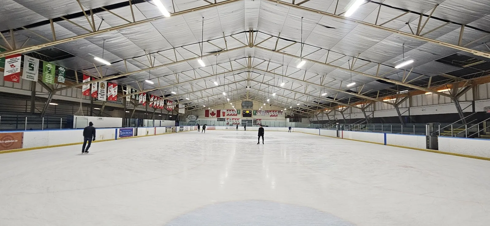 A long empty sheet of ice under a steel-trussed roof, a lone skater far down the ice and banners and Canadian flags hung along the far wall. — Central Arena
