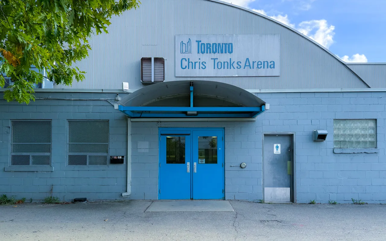 The arena's blue-doored front entrance under an arched metal roof, with a wall sign reading "Toronto Chris Tonks Arena" above the doorway. — Chris Tonks Arena