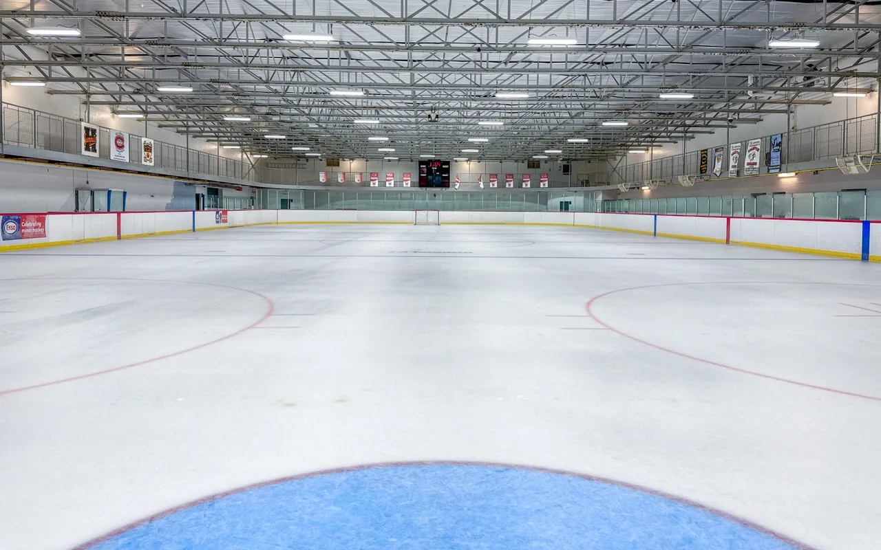 Pista de hielo vacía del Cummer Park Community Recreation Centre vista desde el nivel del hielo, con las vigas de acero del techo y las vallas a los lados. — Cummer Park Community Centre