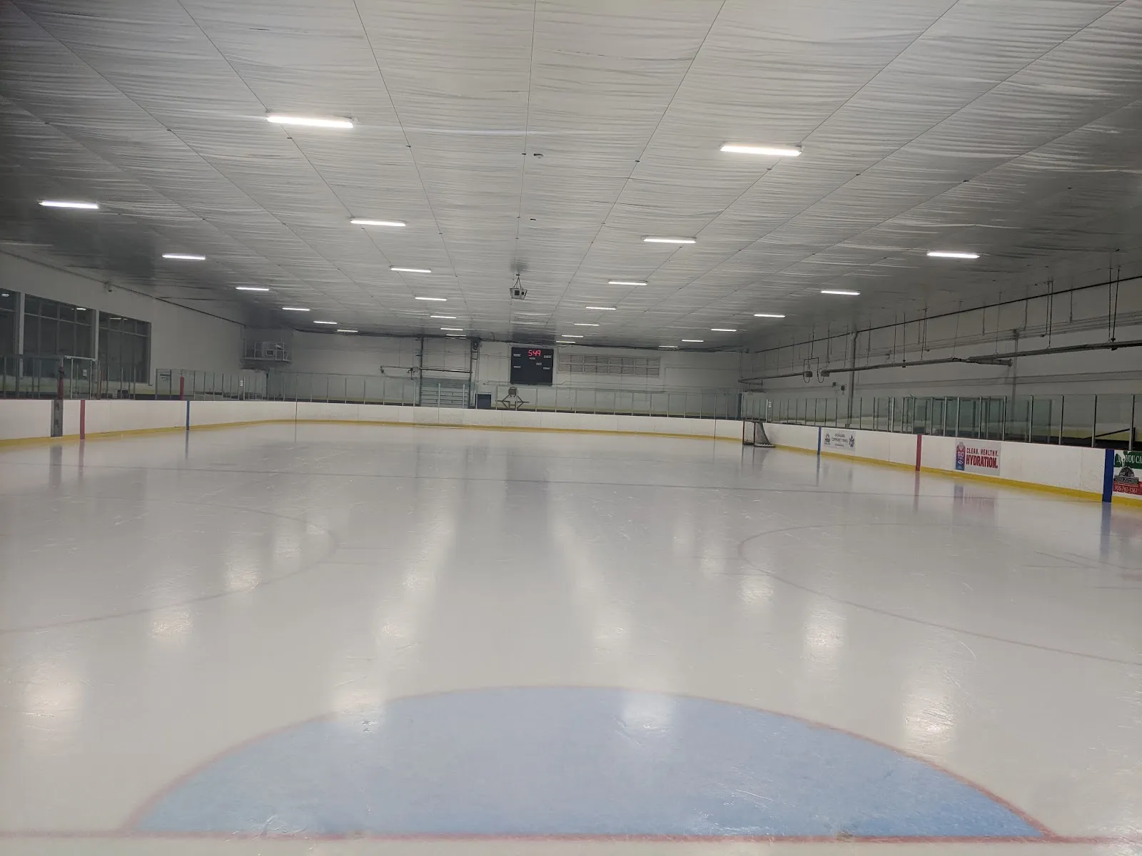 Empty Goulding arena ice sheet viewed from ice level toward the far boards, scoreboard and rink signage; no skaters present. — Goulding Community Recreation Centre