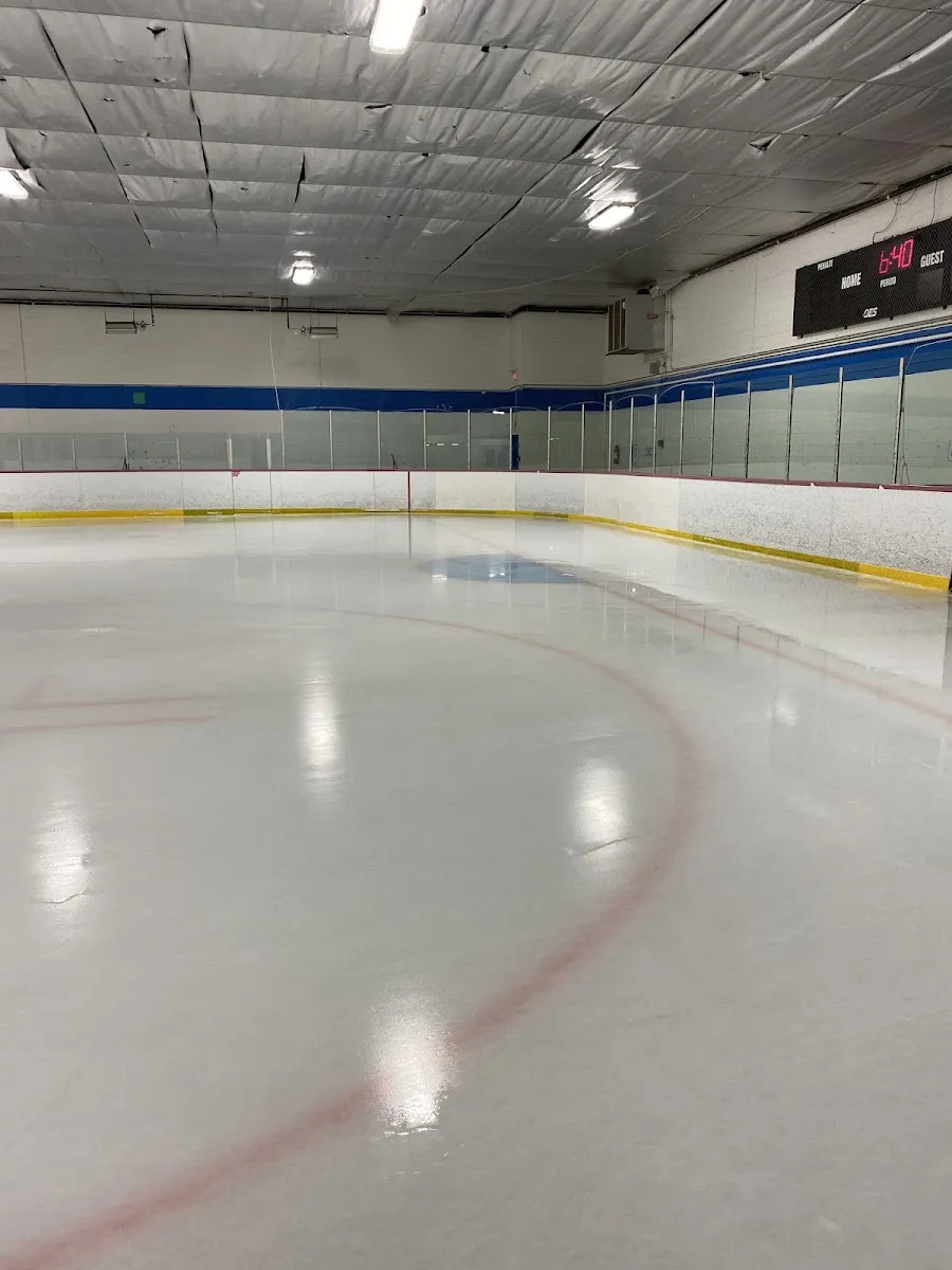 Empty ice sheet at Habitant Arena, viewed from ice level toward the scoreboard end, with red and blue lines and dasher boards visible. — Habitant Arena