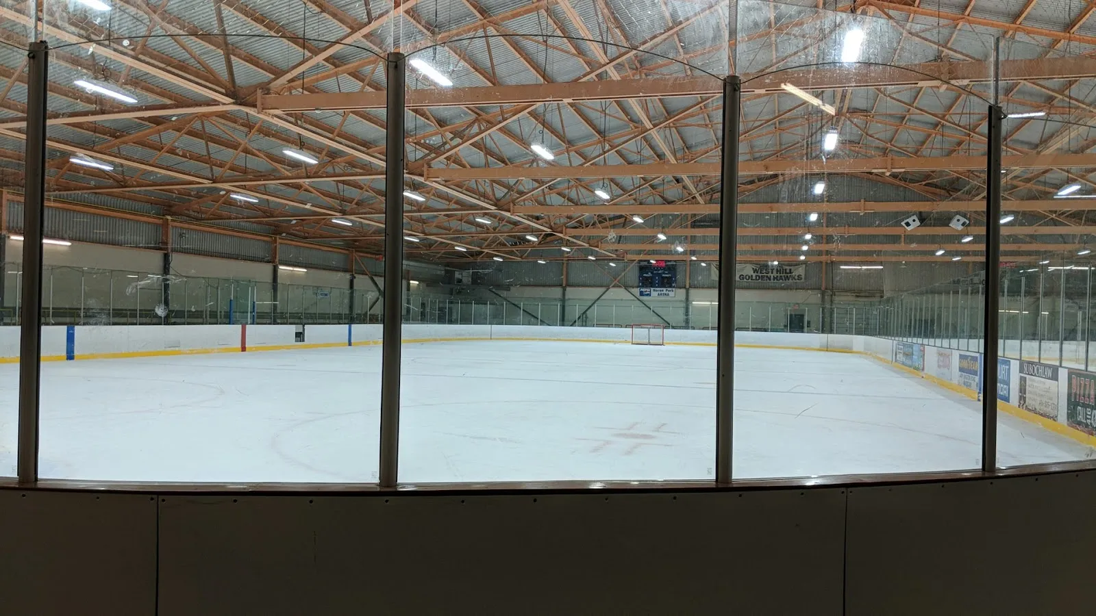 Toda la pista de Heron Park Arena vista a través del cristal, con un letrero en la pared que dice "Heron Park Arena" y una manta de los "West Hill Golden Hawks" sobre las vallas. — Heron Park Community Recreation Centre
