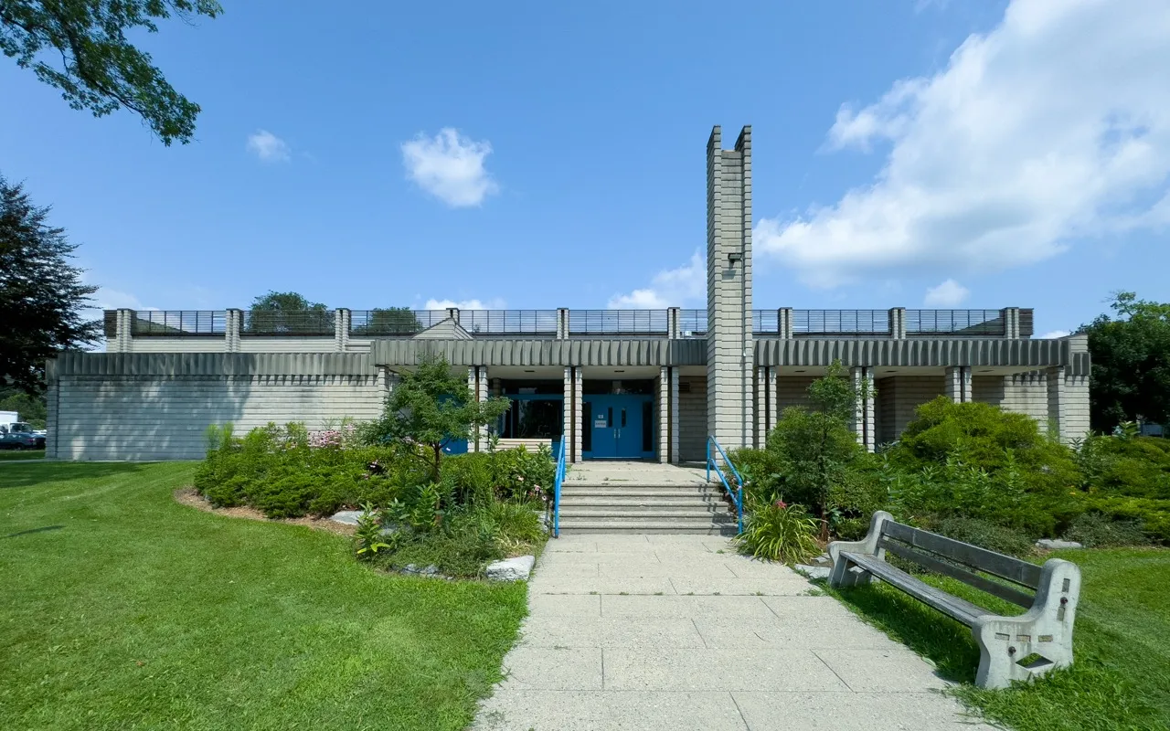 Front entrance to Lambton Arena, a low modern building with a tall slender tower, reached by a stepped path through shrubs. — Lambton Arena