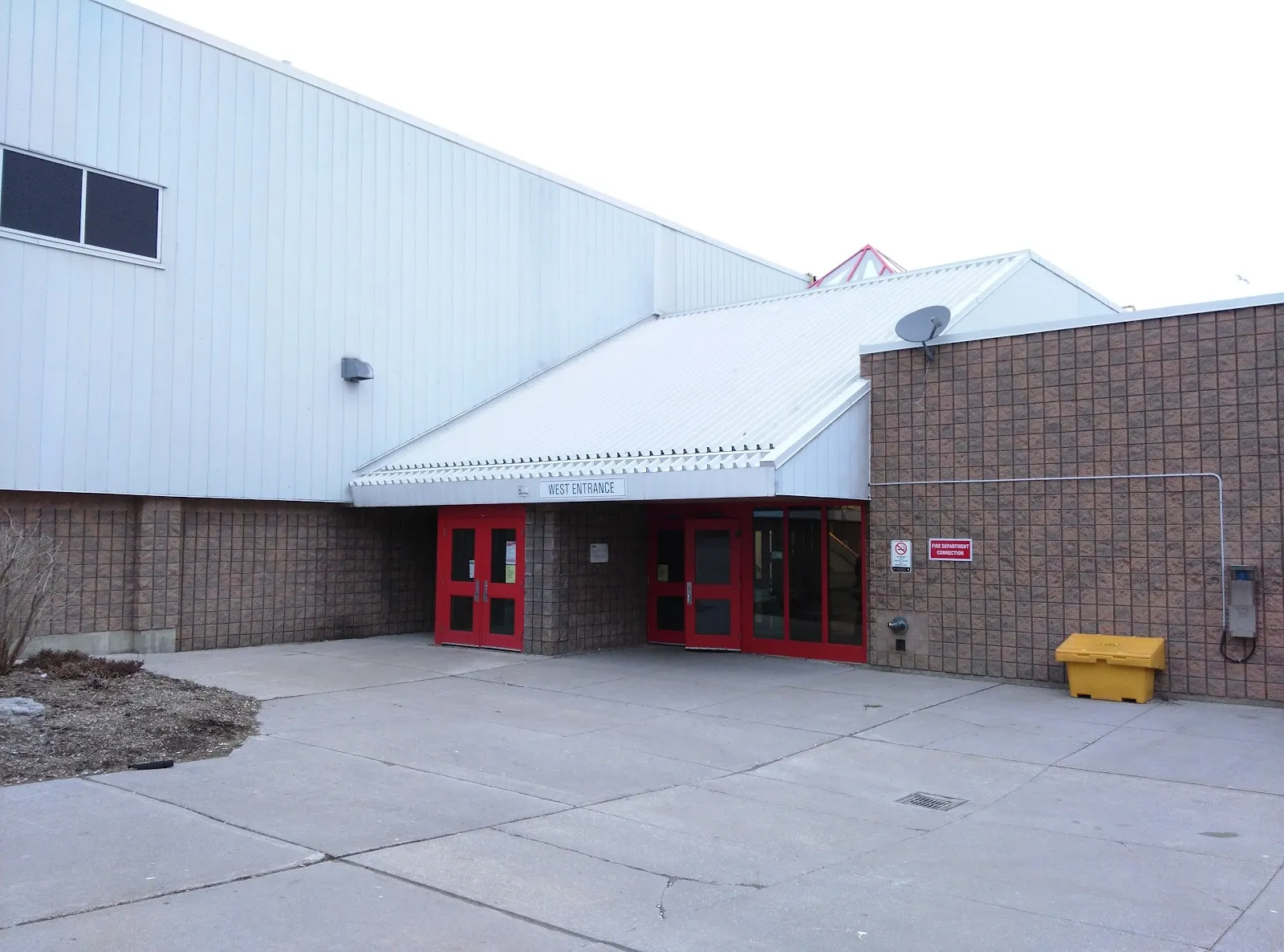 La entrada oeste del Malvern Community Recreation Centre en Scarborough, con sus puertas rojas bajo un techo metálico inclinado y muros de ladrillo — Malvern Recreation Centre