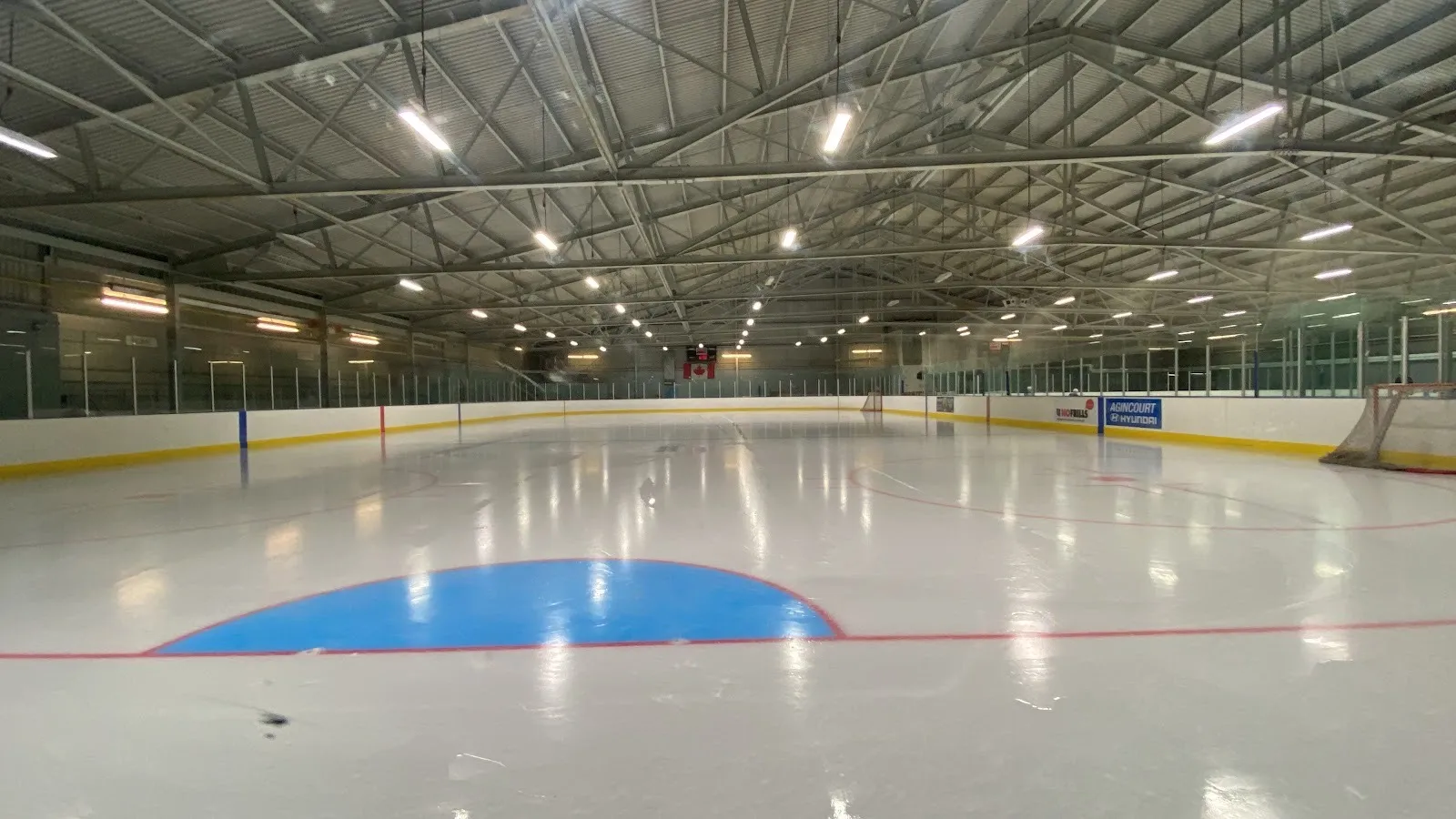 The empty ice at the McGregor Park Community Centre in Scarborough, seen from rink level under the steel roof trusses — McGregor Park Community Centre