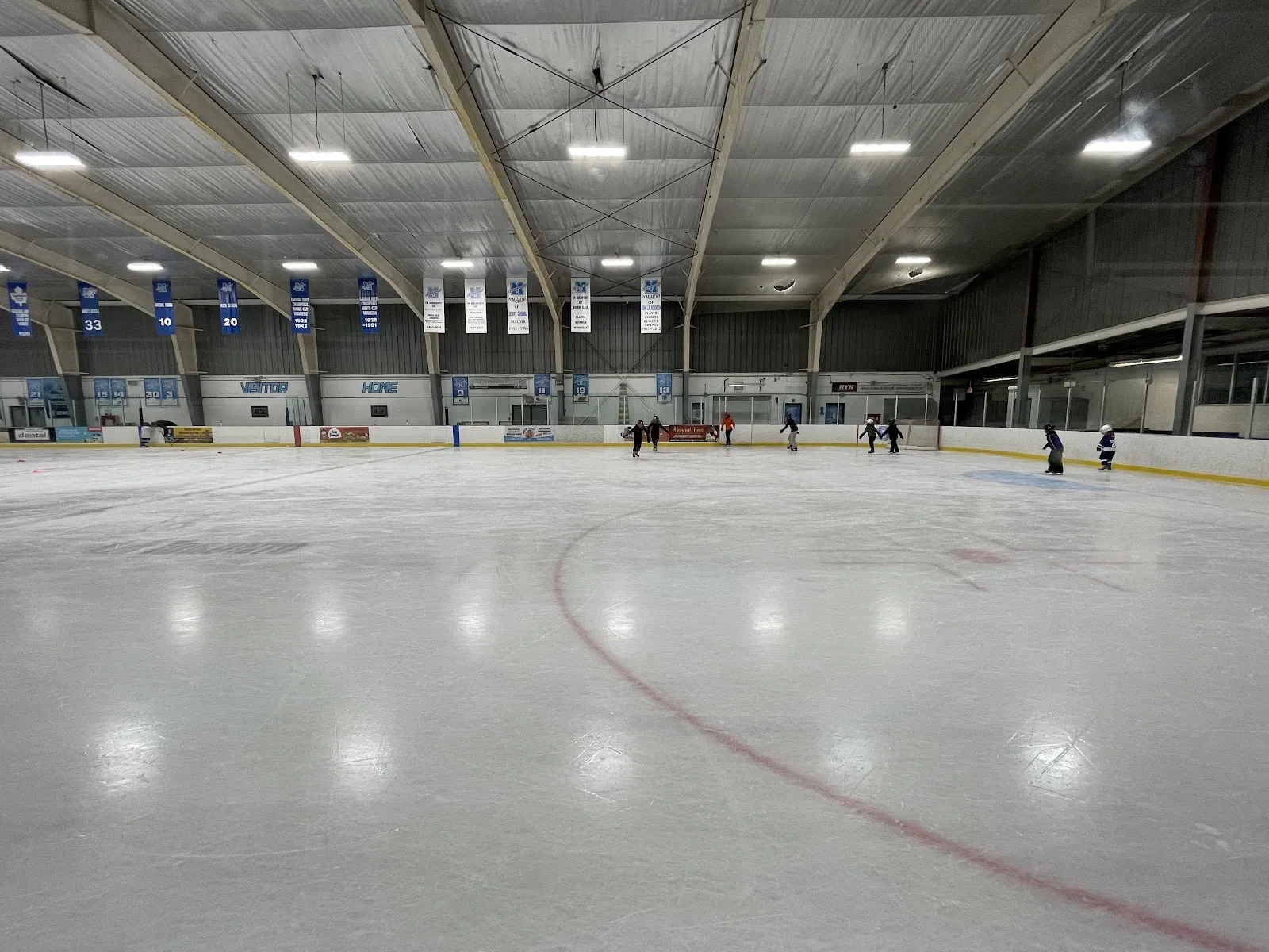 The ice at the Mimico Arena in Etobicoke from rink level, with banners hanging from the roof beams and a handful of skaters — Mimico Arena