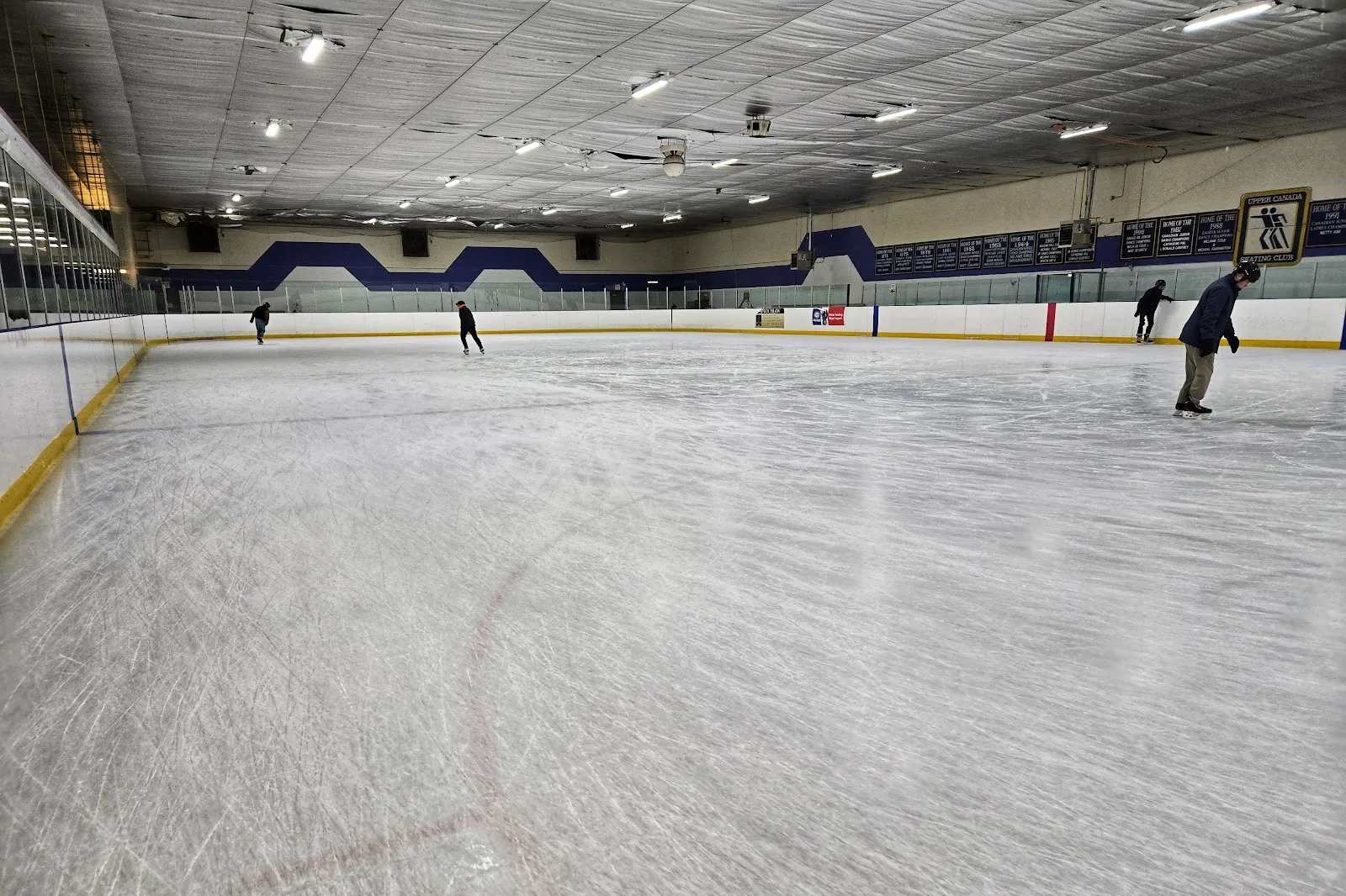 A quiet public skate at the Mitchell Field Community Centre in North York, with a few skaters spread across the scuffed ice — Mitchell Field Community Centre