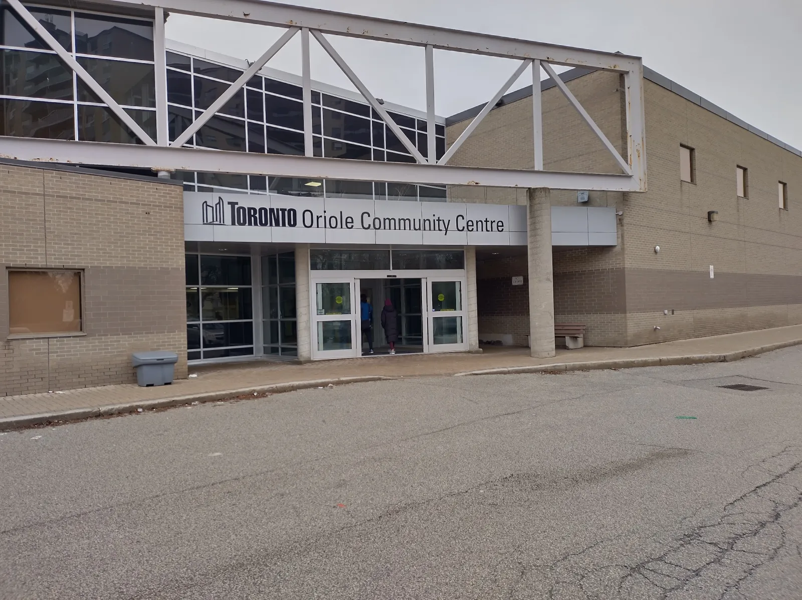 La entrada principal del edificio de ladrillo color arena, con el letrero de Toronto Oriole Community Centre sobre puertas de vidrio y una armadura blanca de acero a lo largo de la orilla del techo. — Oriole Community Recreation Centre